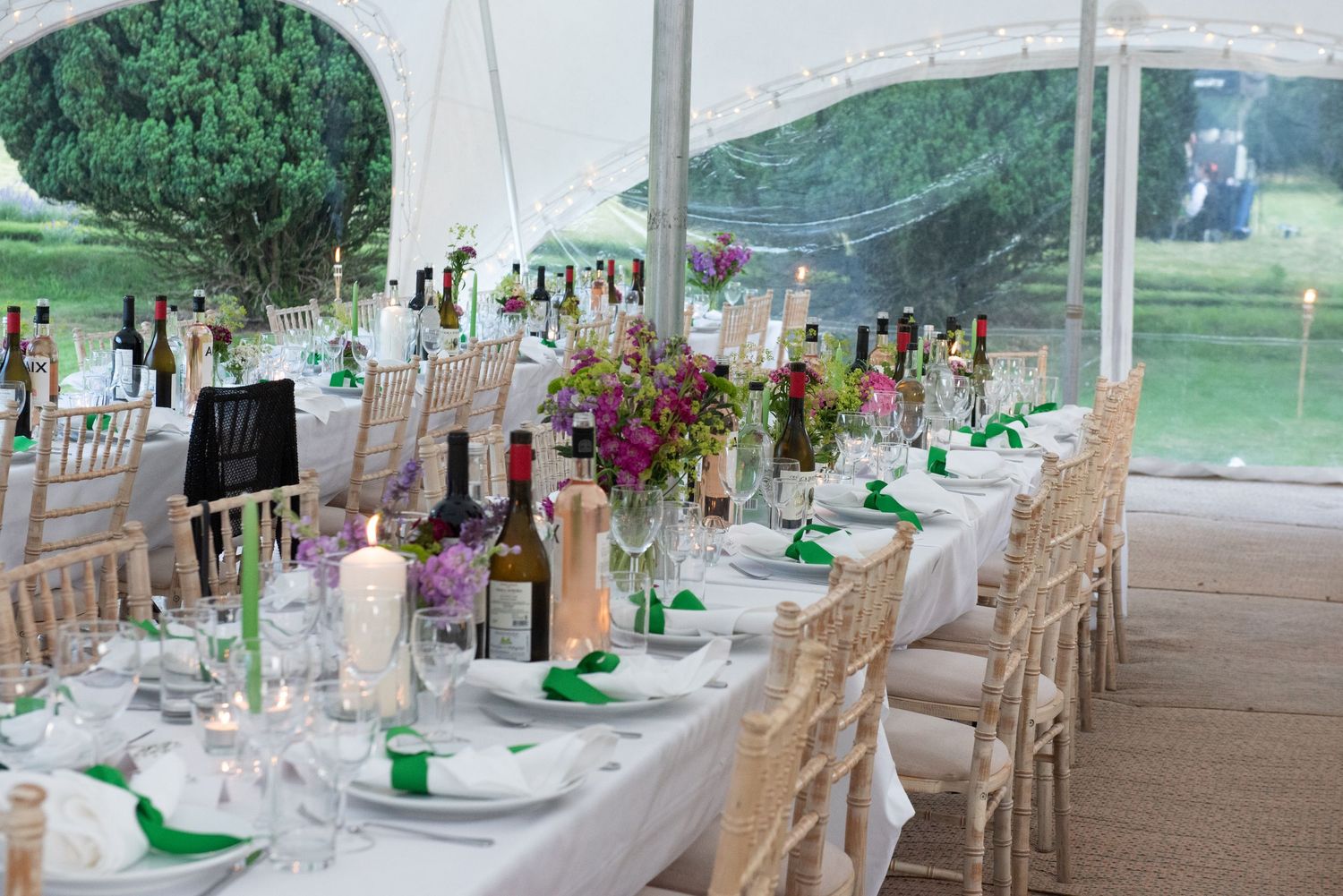 Elegant wedding reception tent with long tables set with green napkins, candles, and floral centerpieces.