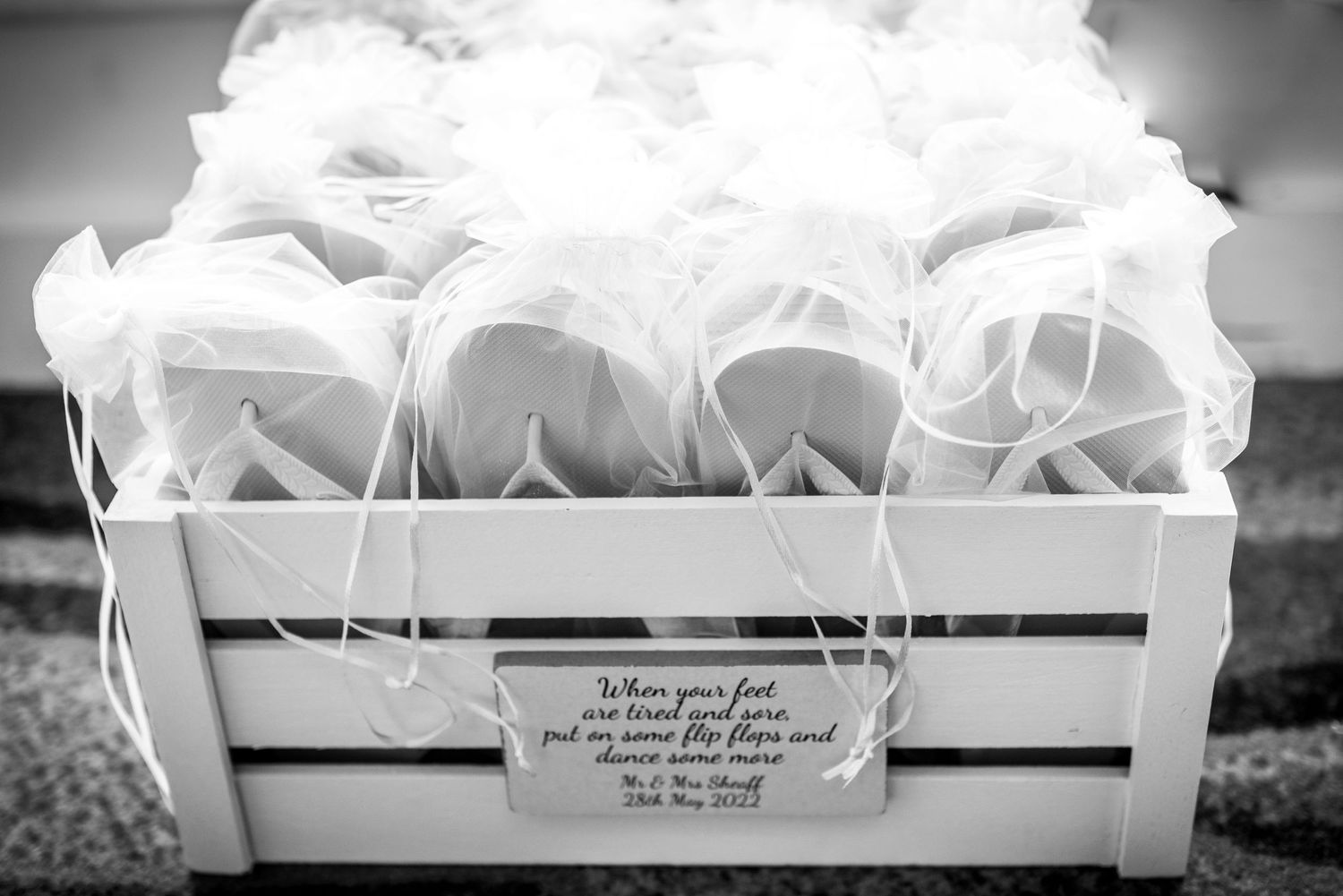 Black and white photo of a crate filled with flip flops for wedding guests to wear.