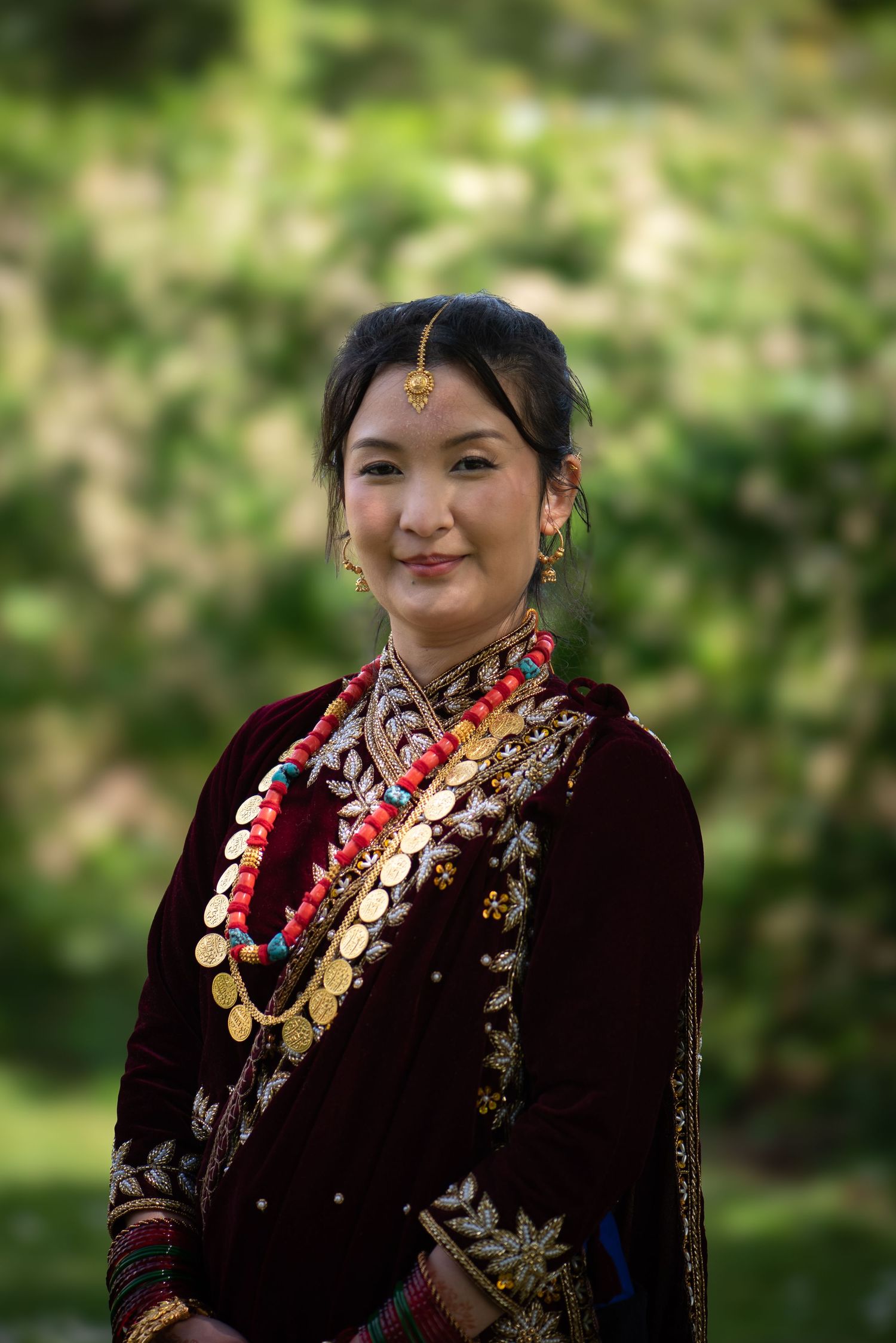 Young woman in traditional Nepali attire with gold coin necklace and red beads smiles outdoors.