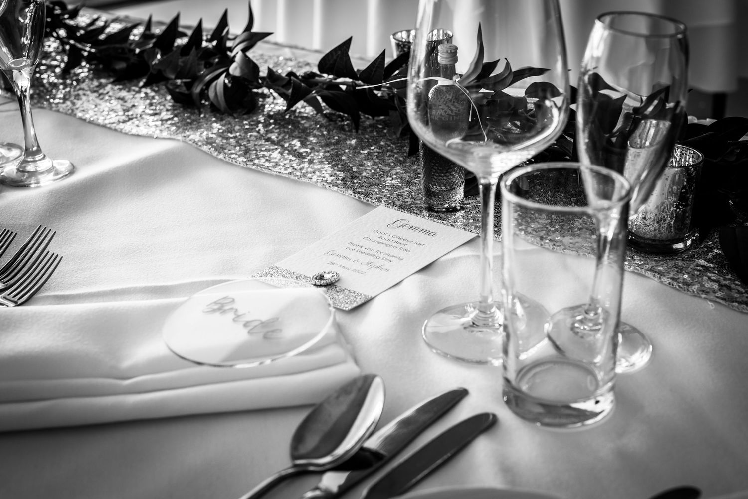 Elegant black and white wedding table setting with wine glasses, cutlery, and floral centerpiece.