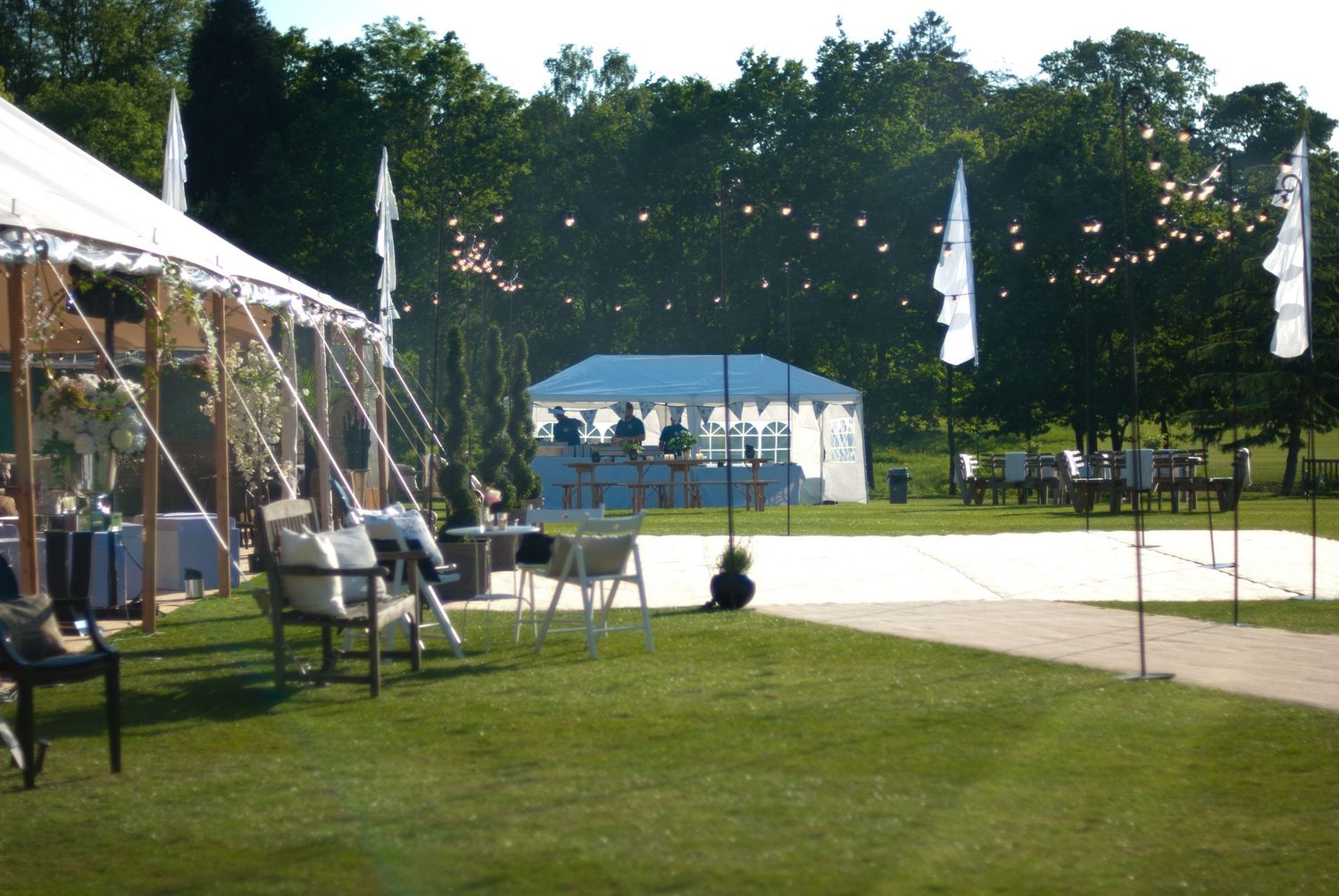 Outdoor party venue with white marquee tents and festoon lights on a sunny day.