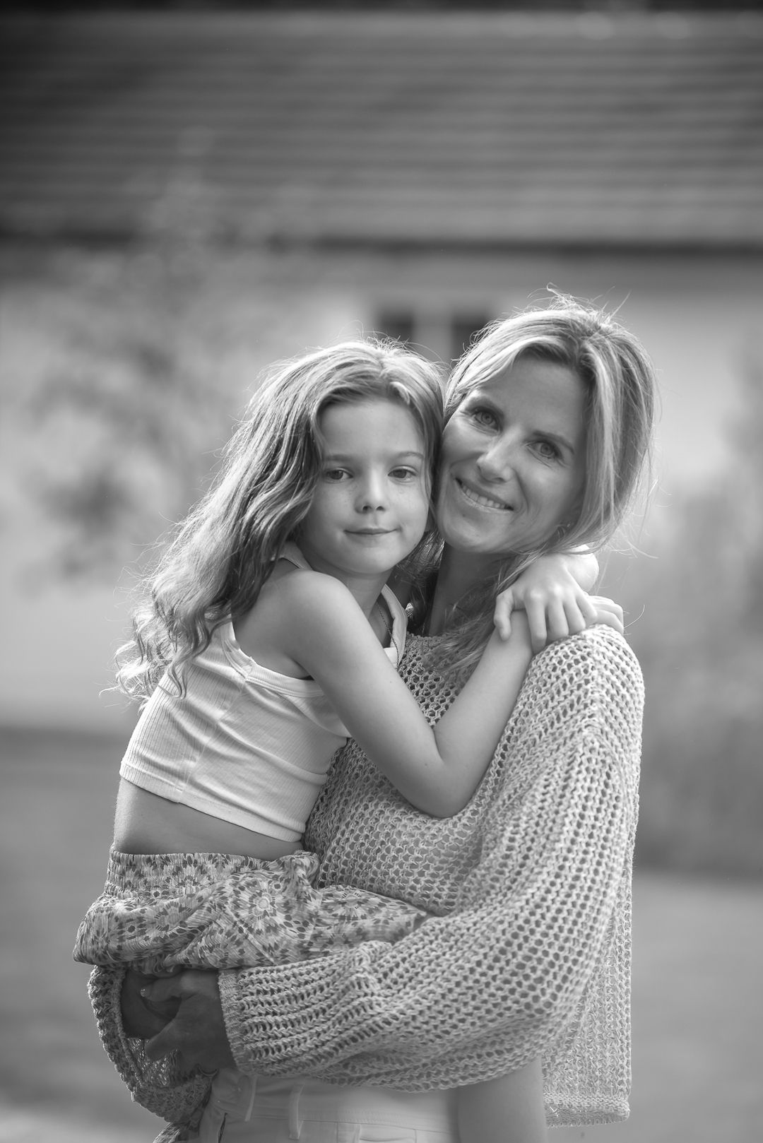Mother hugging young daughter outdoors in black and white portrait photo.