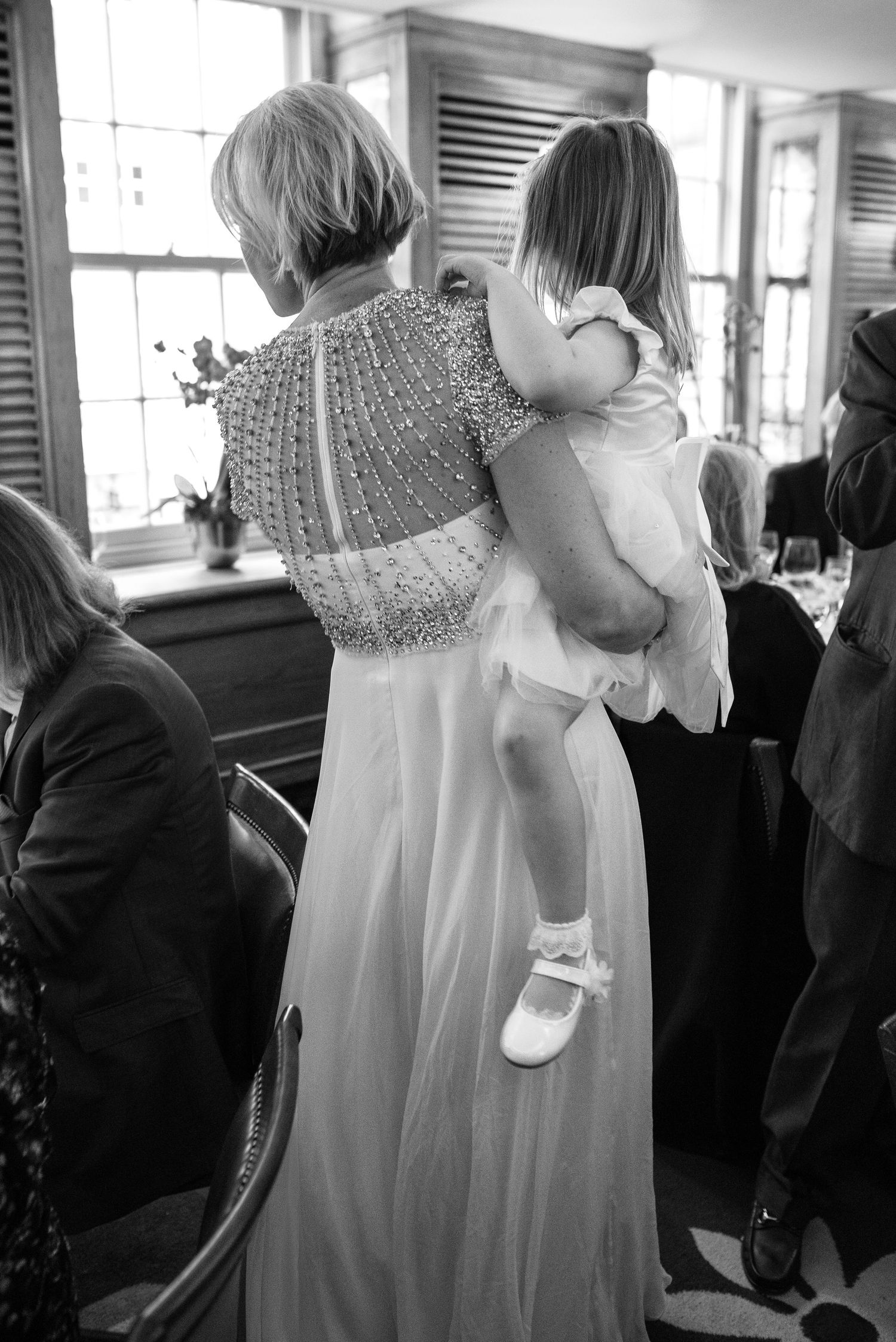 Woman in beaded white gown holding a young flower girl in white dress at a wedding reception.
