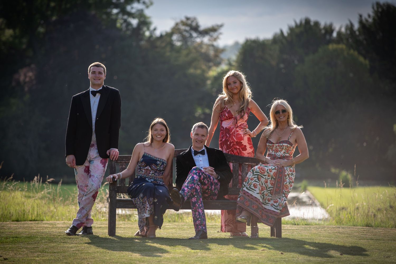 Group of five elegantly dressed guests posing outdoors at golden hour during a garden party event.