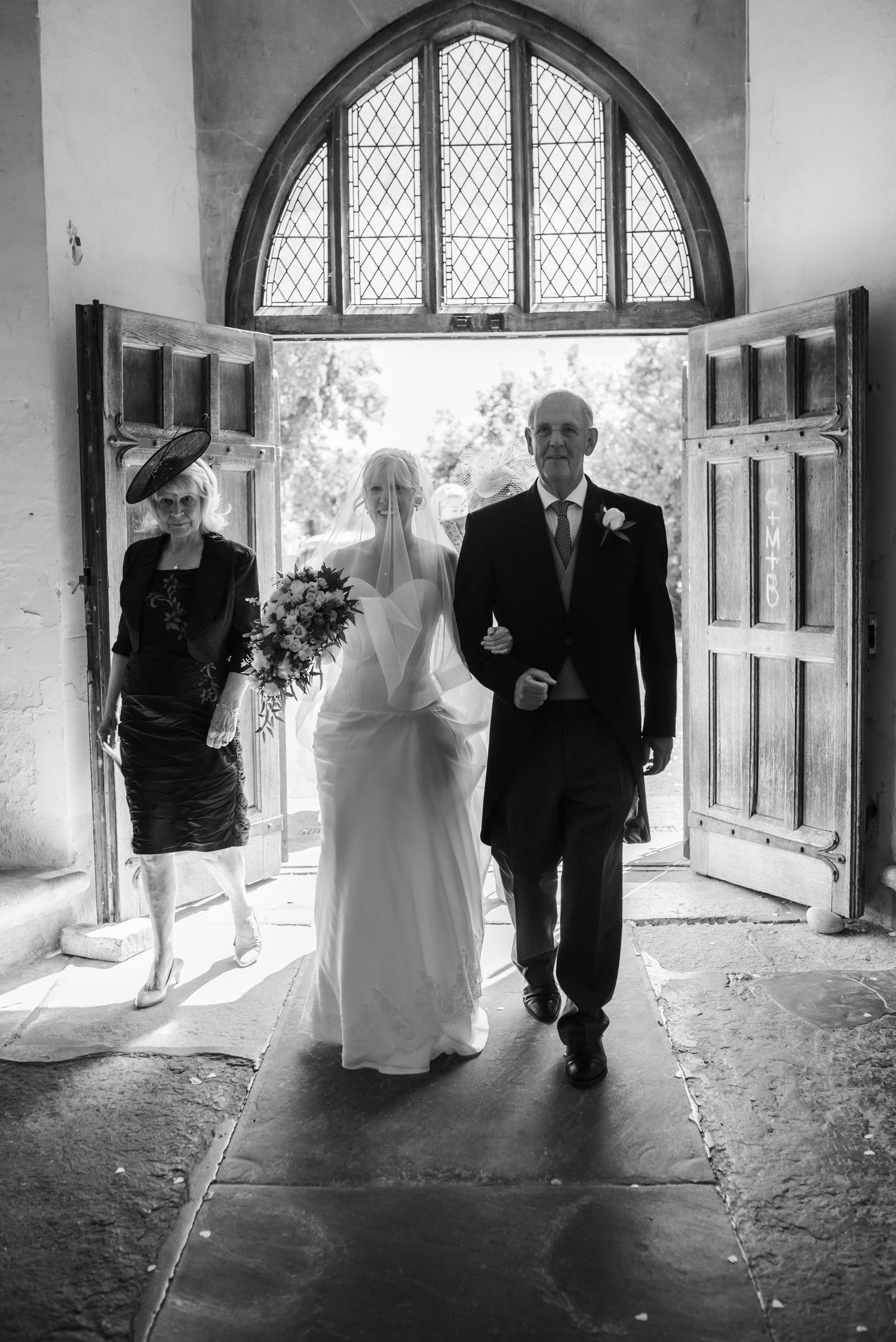 Bride enters a historic church through wooden doors accompanied by her father in black and white. St Michaels Church, Bray