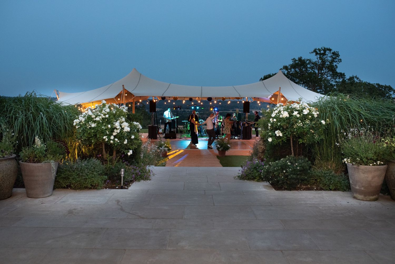 Elegant outdoor wedding reception under a stretch tent with string lights at dusk.