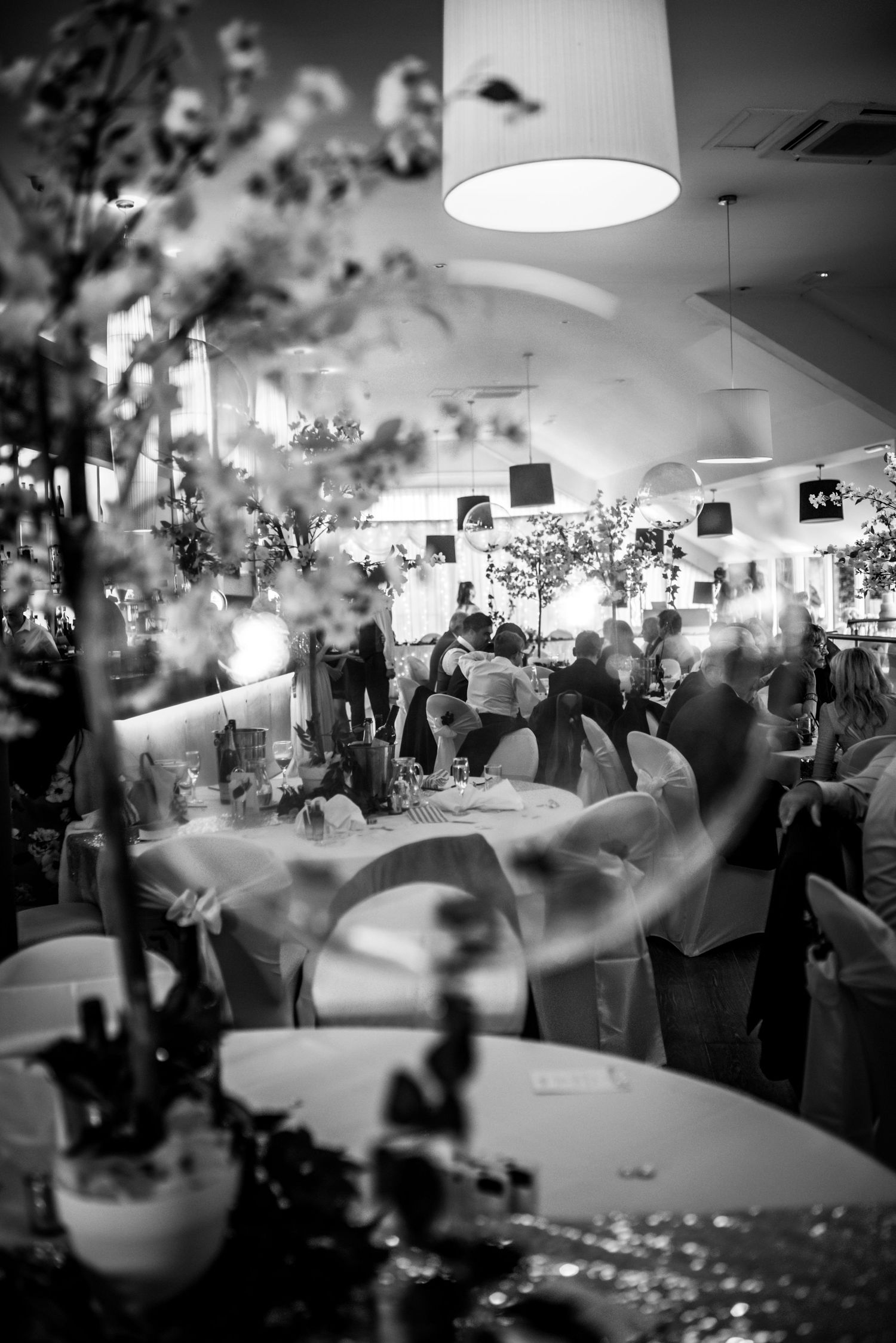 Elegant wedding reception hall with floral centerpieces, white chair covers, and warm ambient lighting.