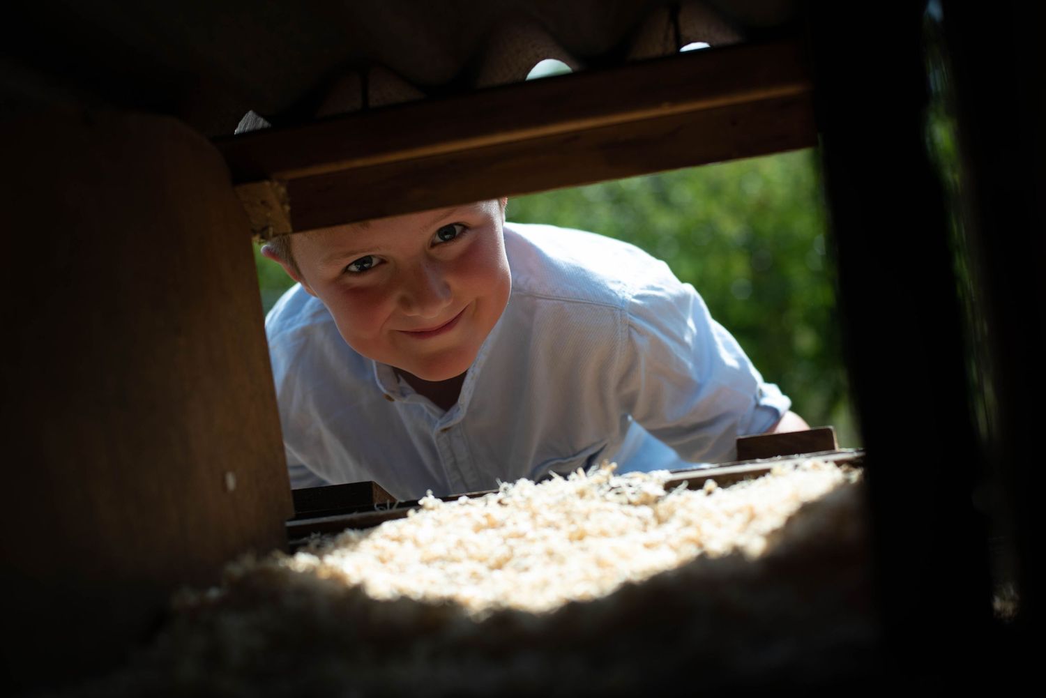 A young boy in a blue shirt peeks playfully under a piece of outdoor furniture.