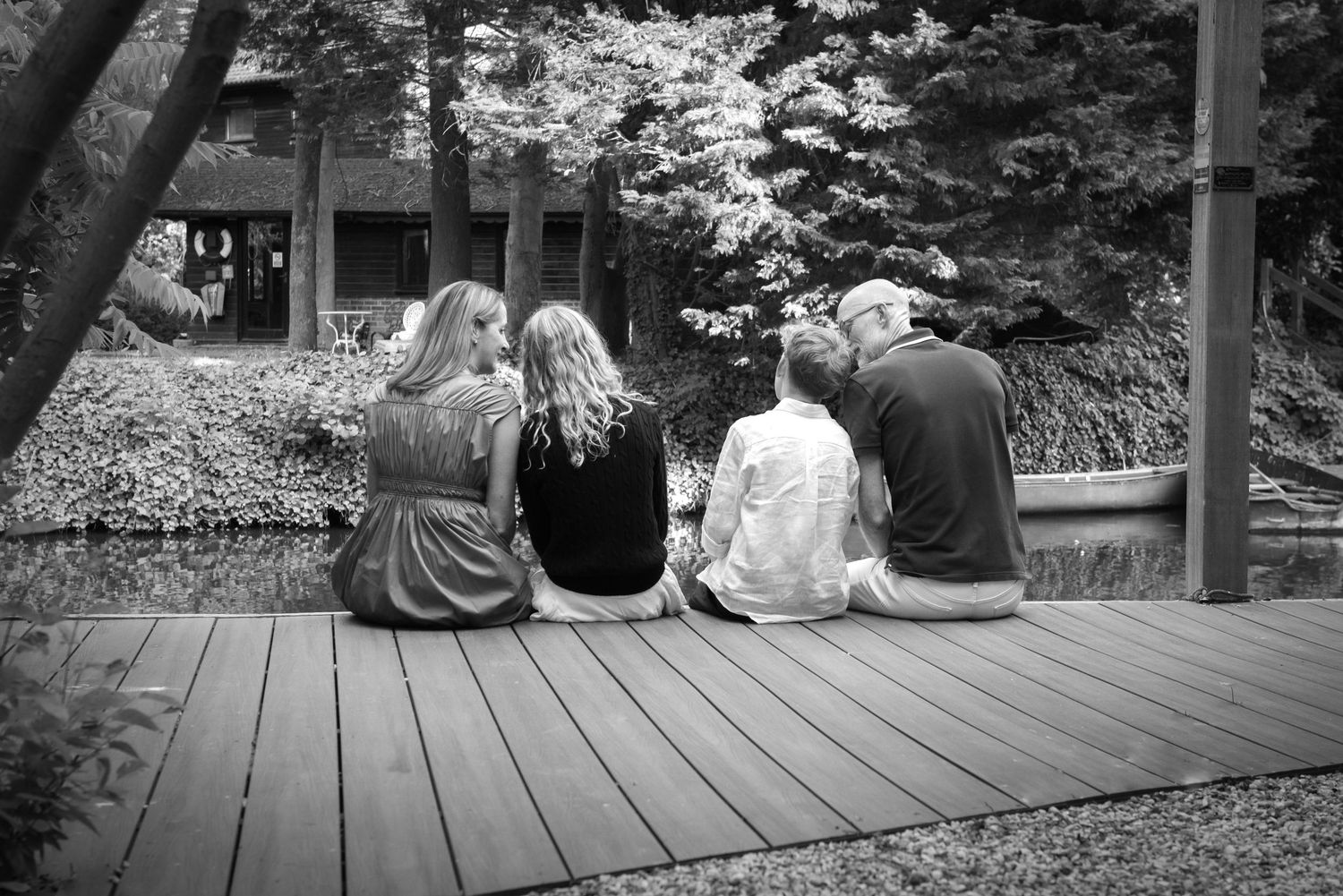Four people sit together on a wooden deck overlooking a tranquil garden pond.