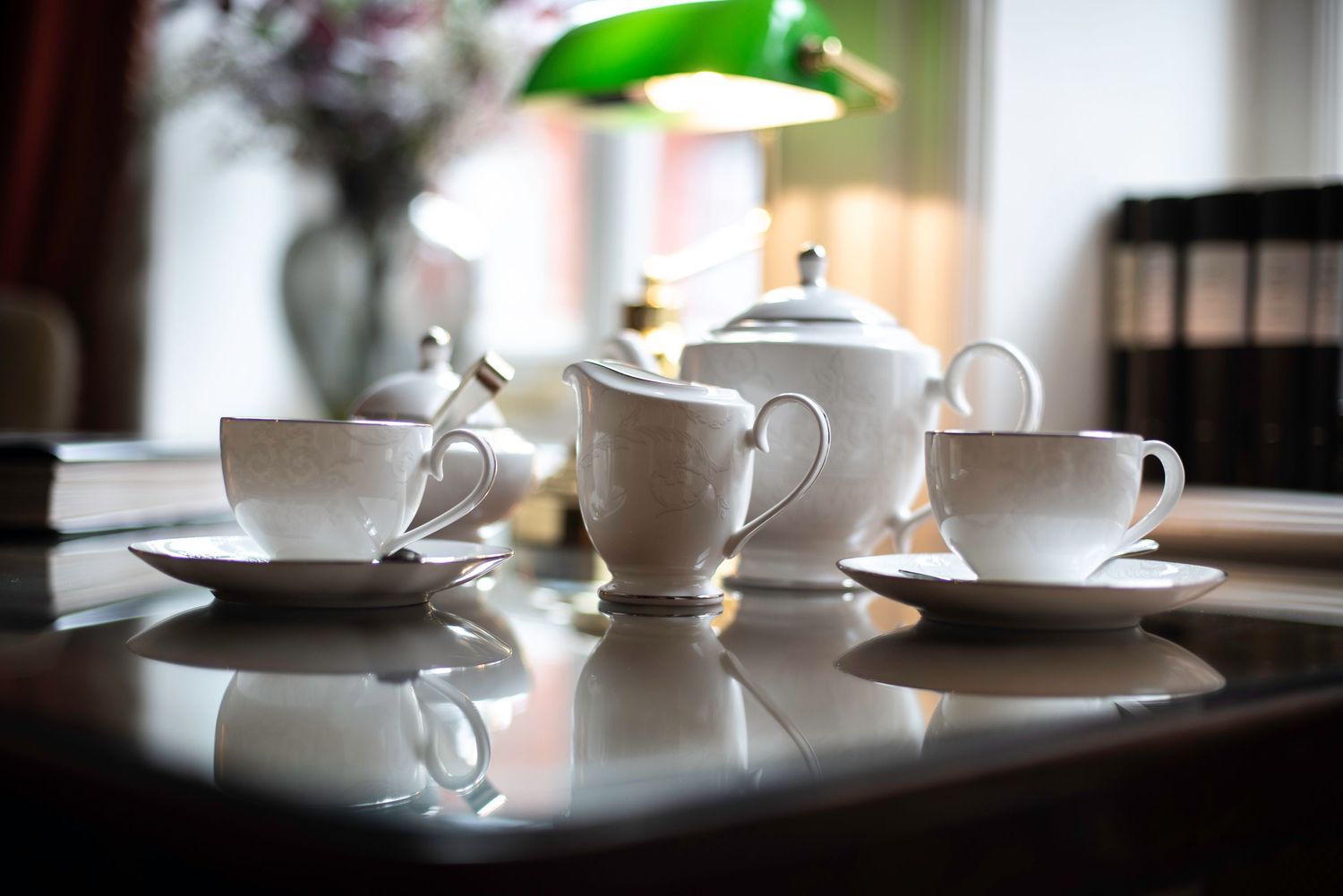 Elegant white porcelain tea set with teapot, cups, and saucers on a reflective wooden table. Draycott Hotel London