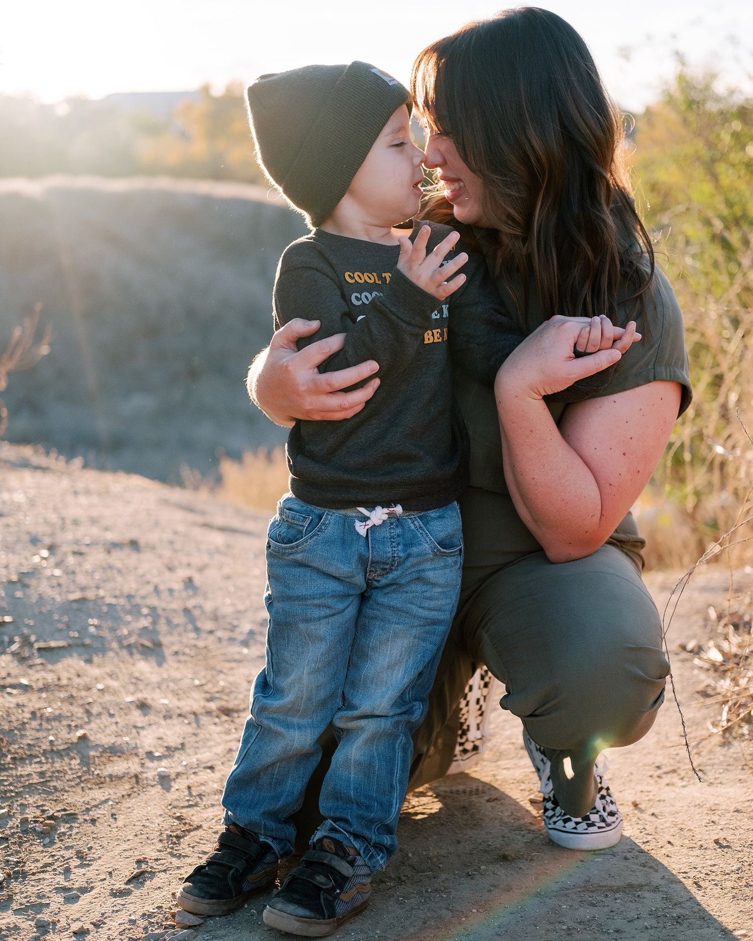 Mother and young son share a tender nose-to-nose moment outdoors at sunset.