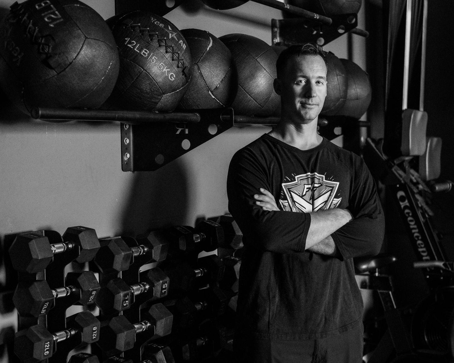 Fit man with crossed arms standing in a gym surrounded by weights and equipment.