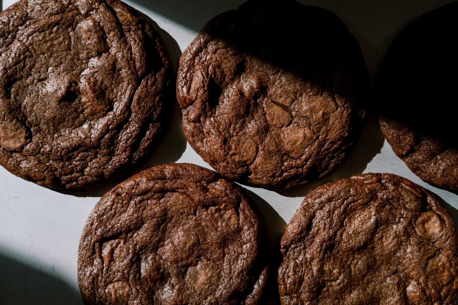 Overhead view of rich, crinkled double chocolate cookies cooling on a white surface.