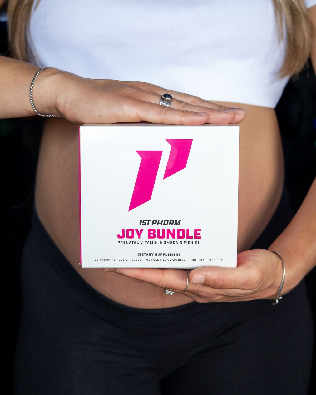 Pregnant woman holding a 1st Phorm Joy Bundle prenatal vitamin and omega-3 supplement box.