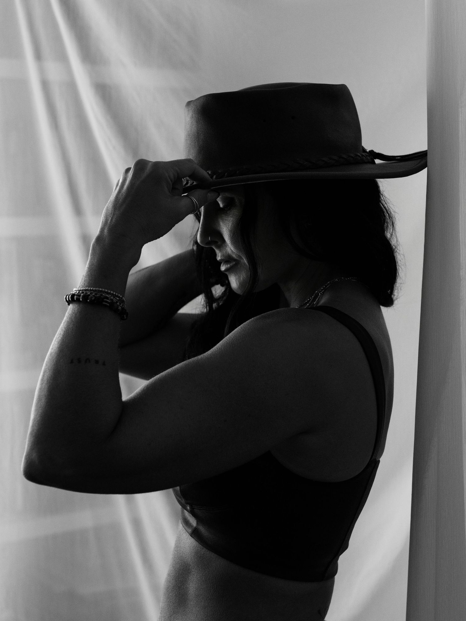 Black and white silhouette of a woman in a crop top adjusting a wide-brim cowboy hat.