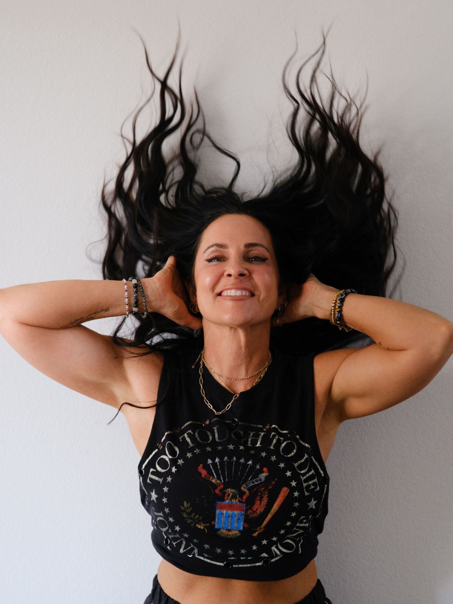 Woman laughing with long dark hair spread out, wearing a black graphic tank top.