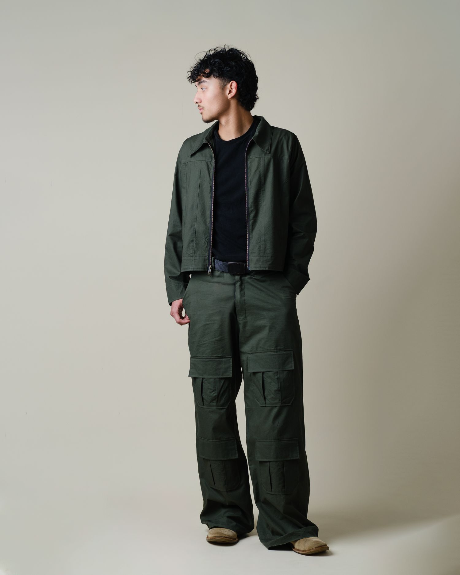 Male model wearing olive green cargo pants and matching jacket standing in studio.