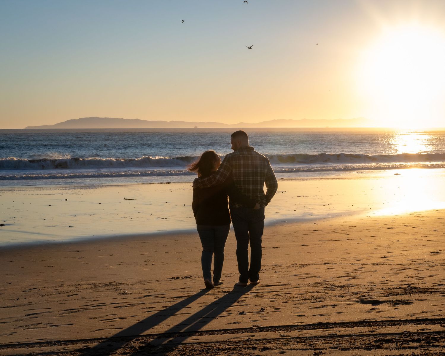 Romantic couple walking hand-in-hand on a beach at golden sunset with ocean waves.