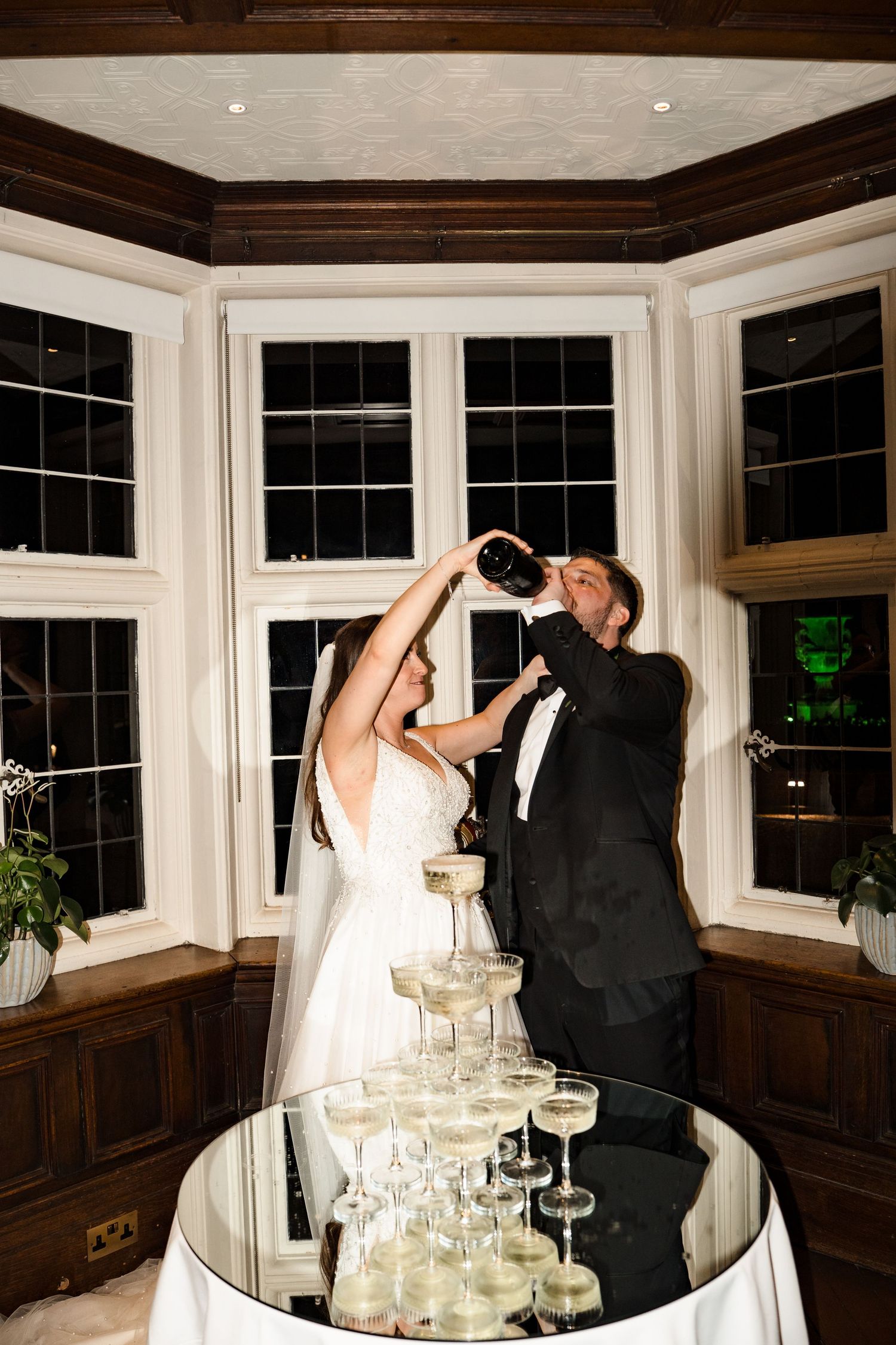 Bride and groom pouring champagne over a tiered champagne tower at their wedding reception.