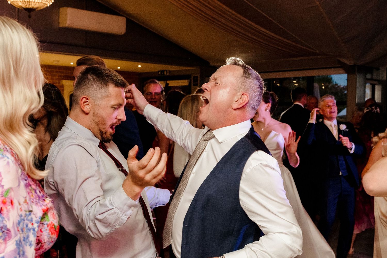 Two men laugh and celebrate energetically on the wedding reception dance floor.