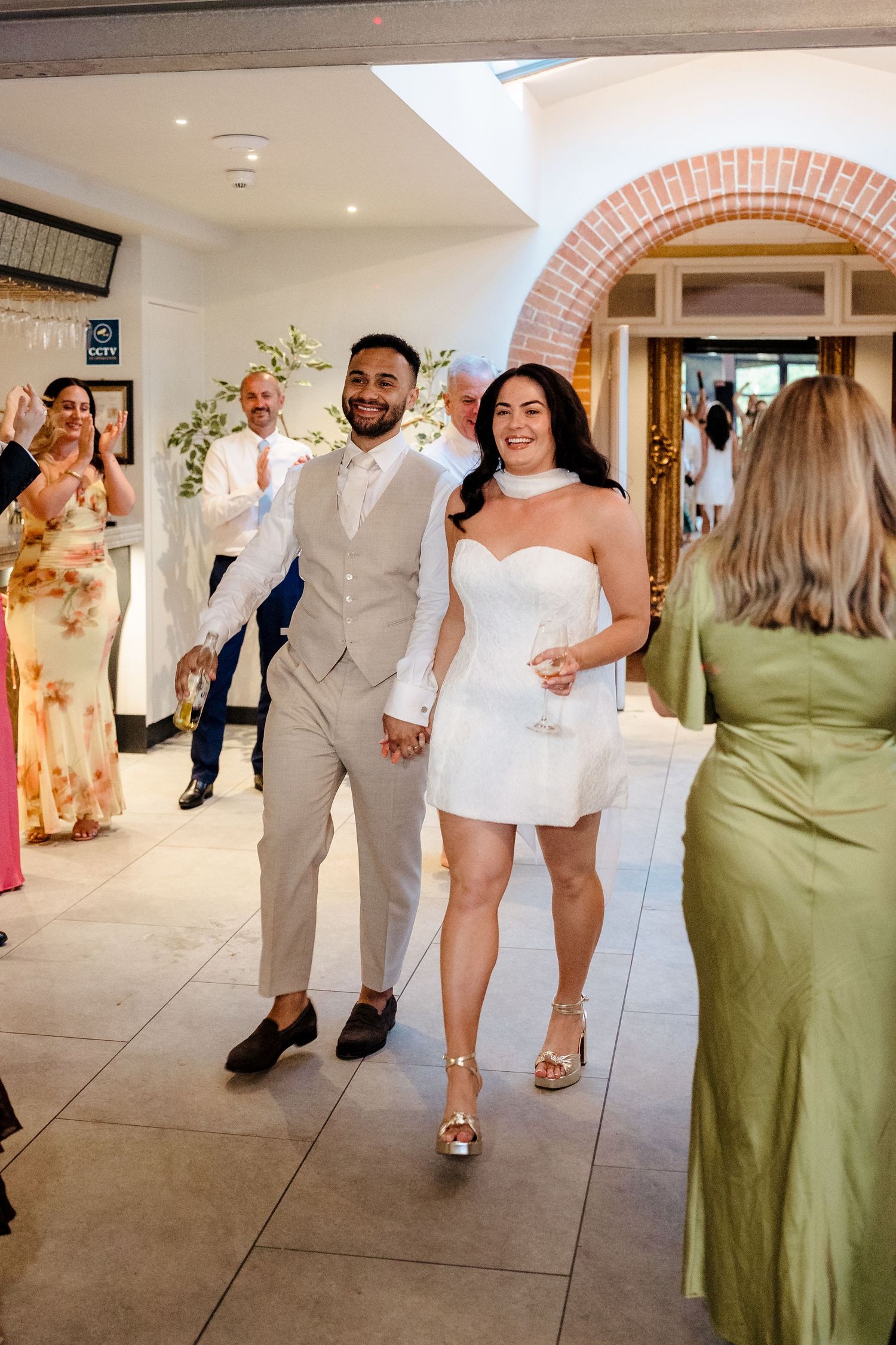 Bride in a short white dress and groom in a tan suit making a grand reception entrance.