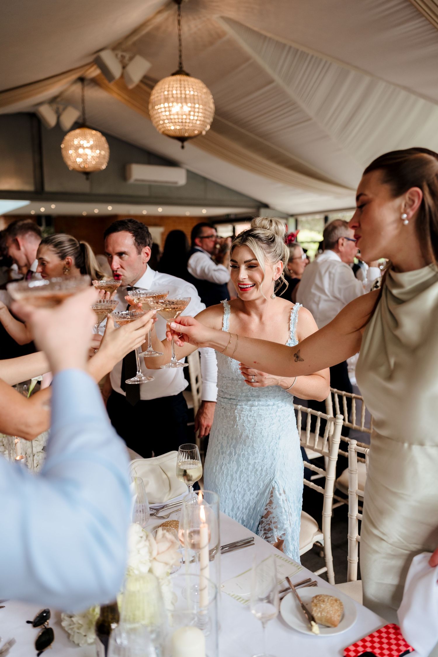 Wedding guests clinking champagne glasses in a toast under a decorated marquee tent.