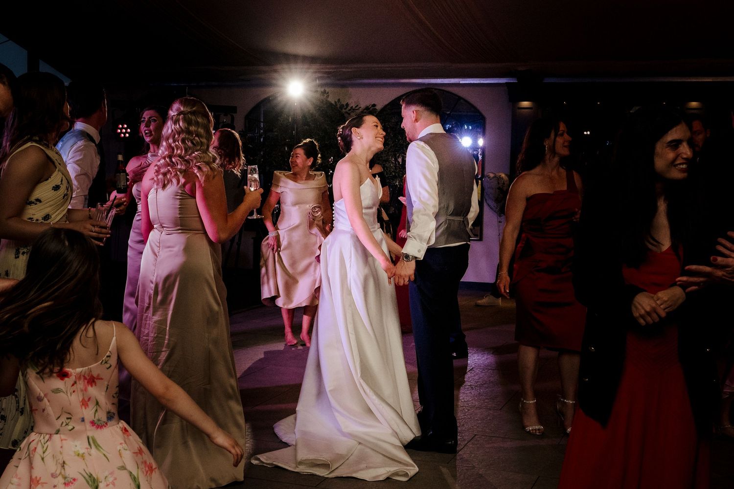 Bride and groom sharing first dance surrounded by guests at evening wedding reception.