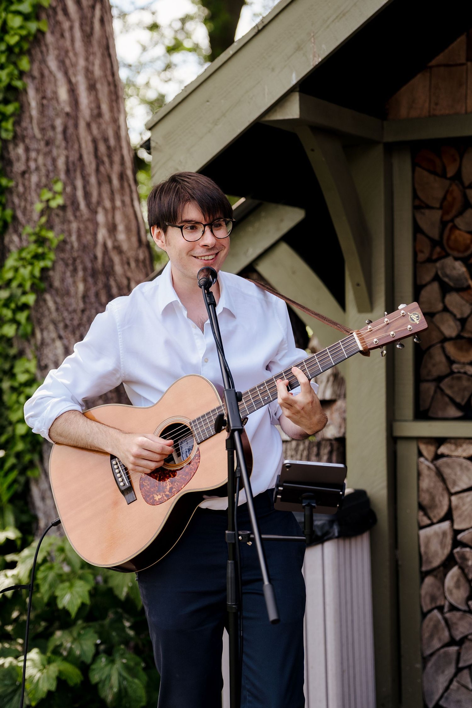 Musician playing acoustic guitar and singing at outdoor wedding ceremony.