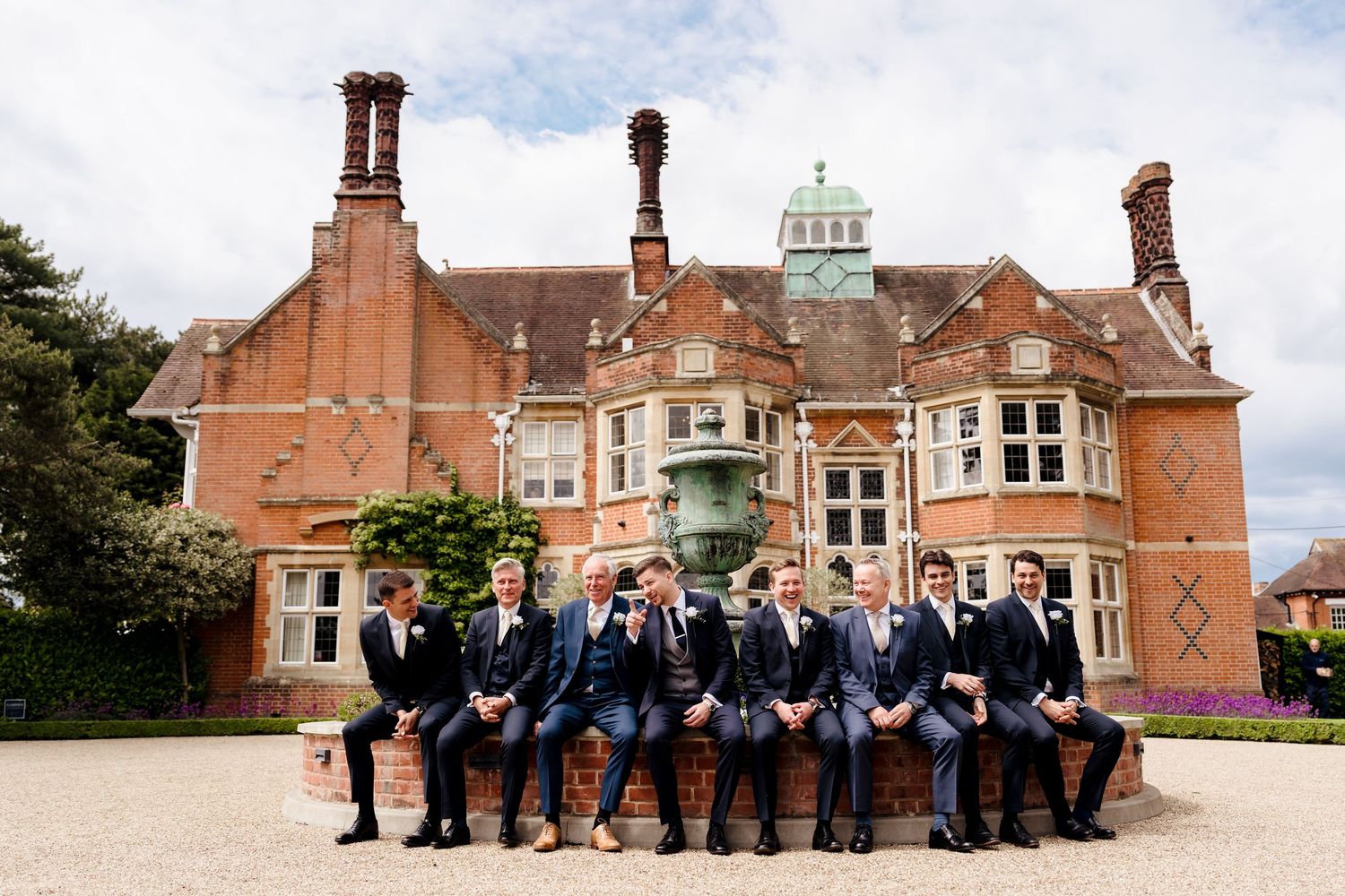 Groom and groomsmen in navy suits posing outside a grand English manor house wedding venue.