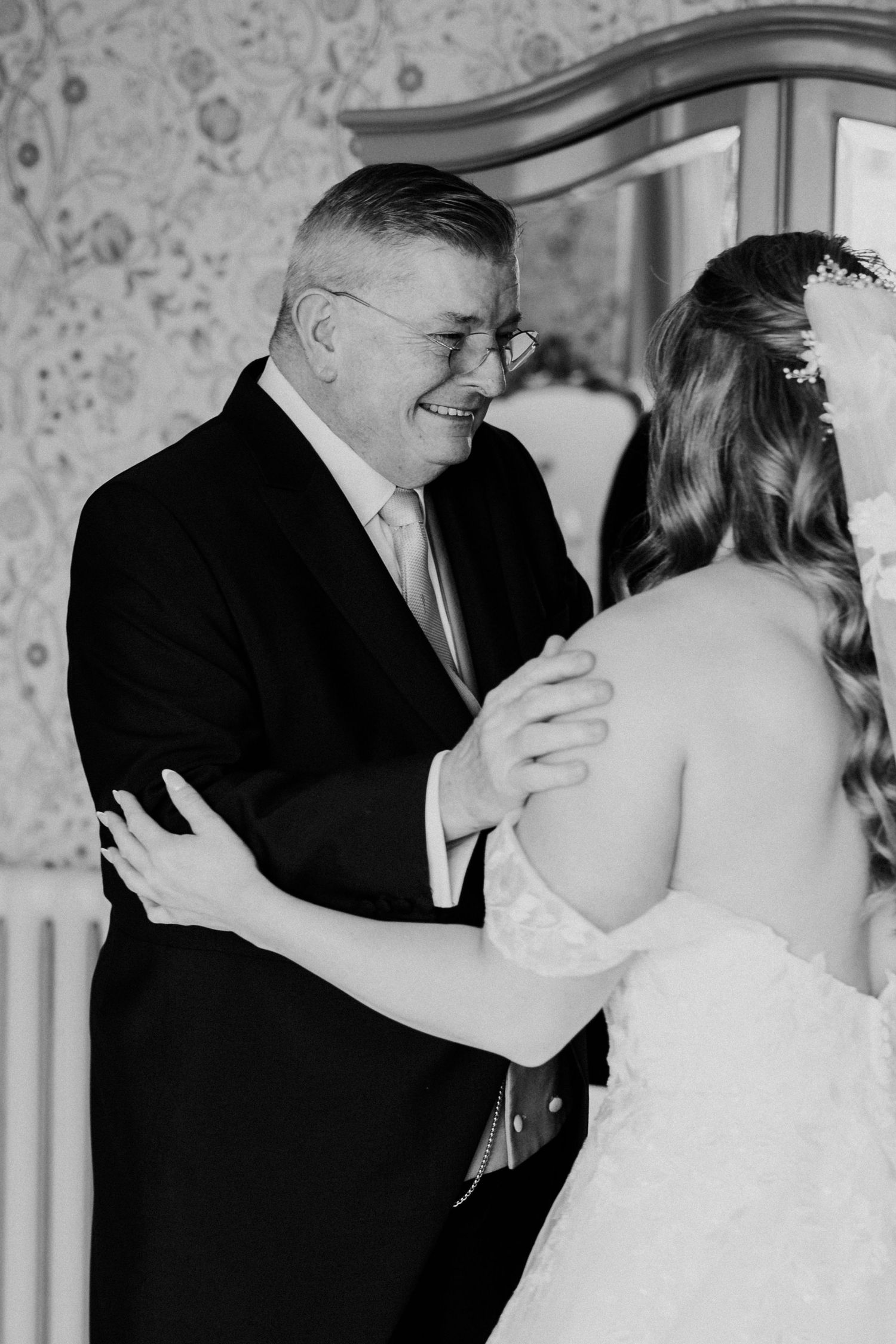 Emotional black and white photo of father seeing bride for first time, sharing a warm embrace and smile.