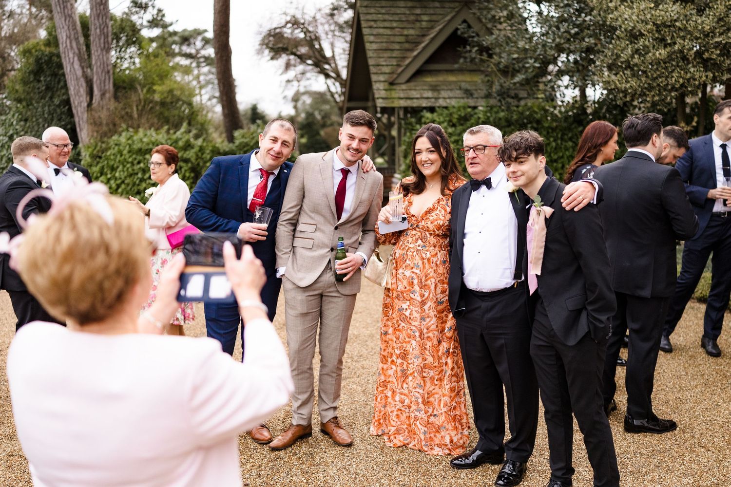 Wedding guests posing for group photo outdoors in garden setting during reception celebration.