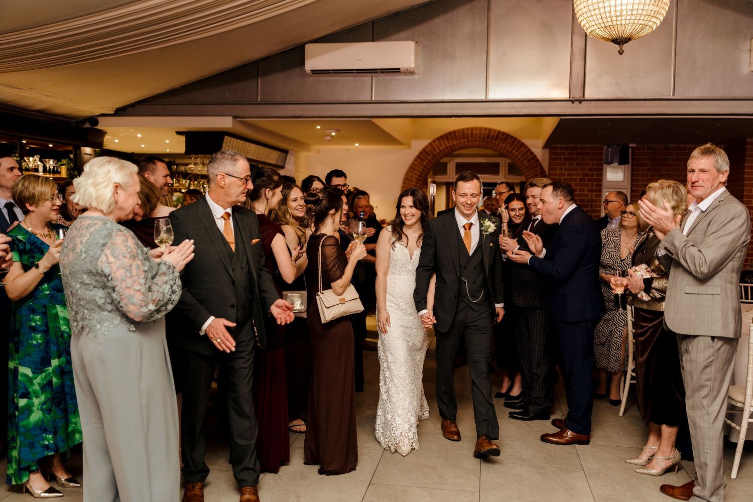 Bride and groom walk through applauding wedding guests in elegant venue during grand entrance reception.