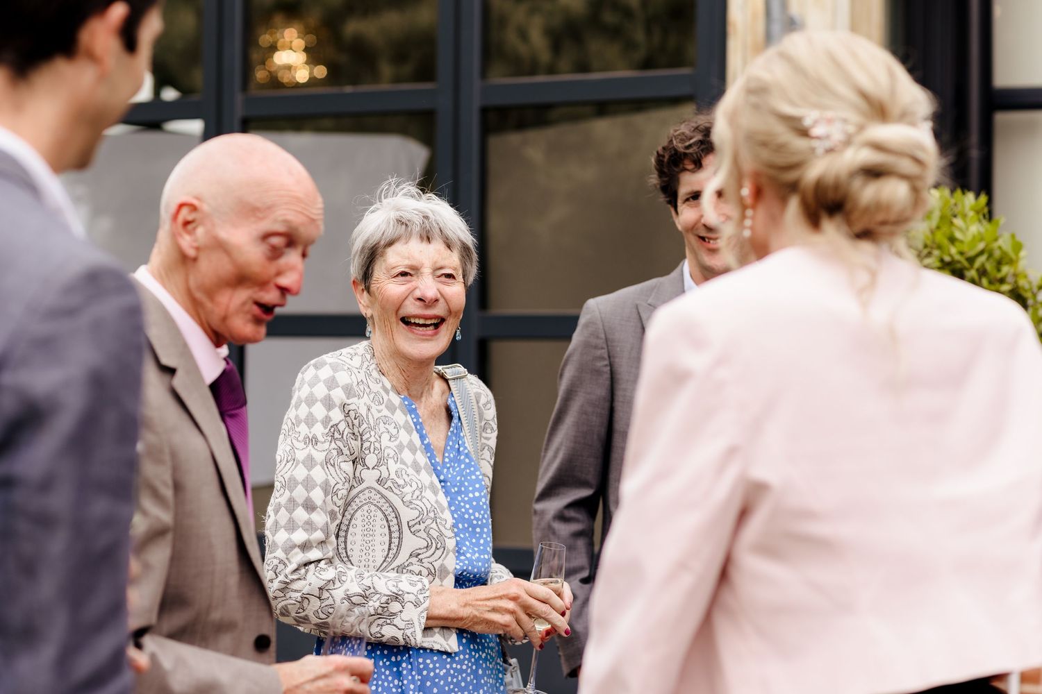 Elderly wedding guests laughing and socializing outdoors at a wedding reception in elegant attire.
