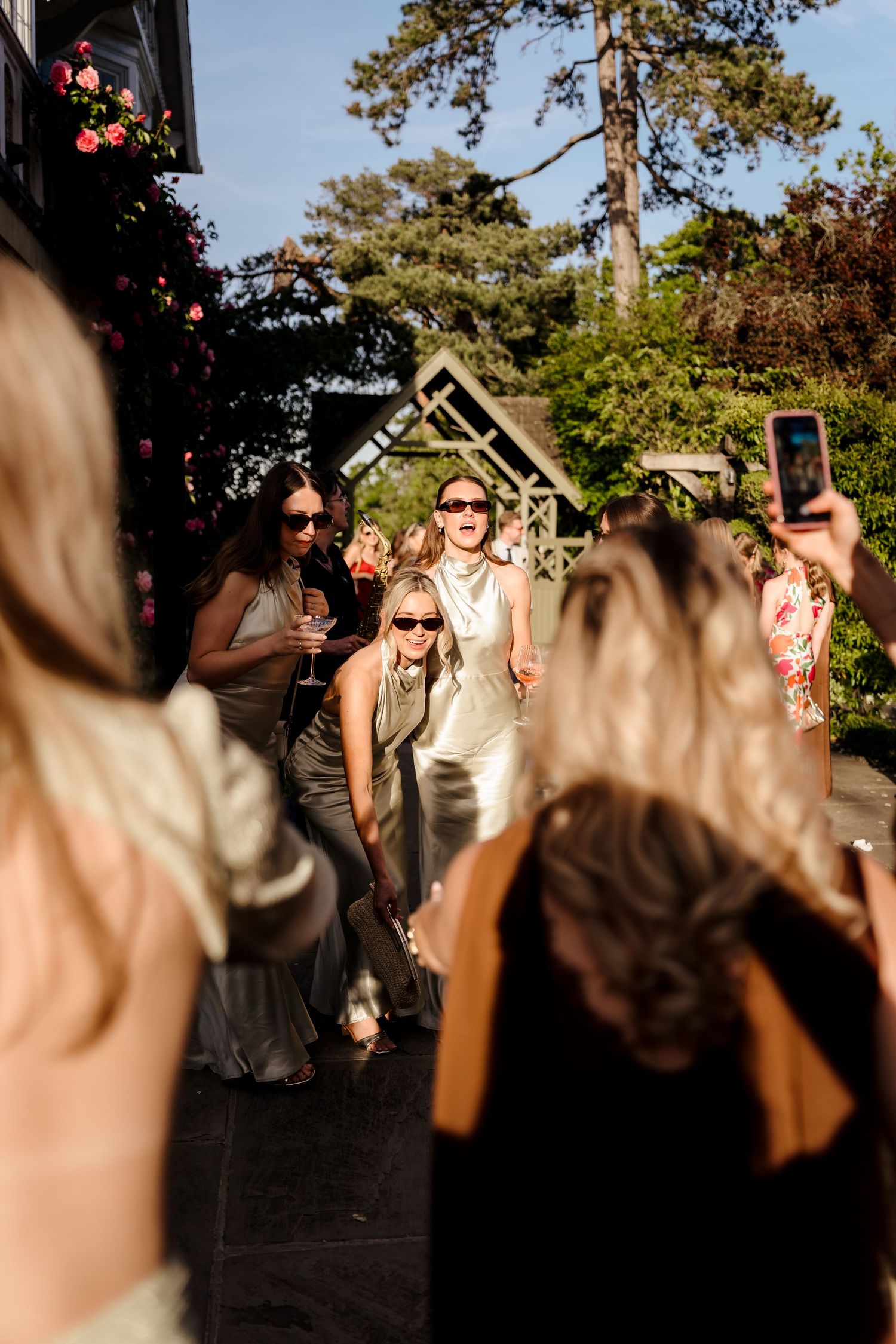 Bride in white dress celebrating with guests at sunny outdoor wedding reception.