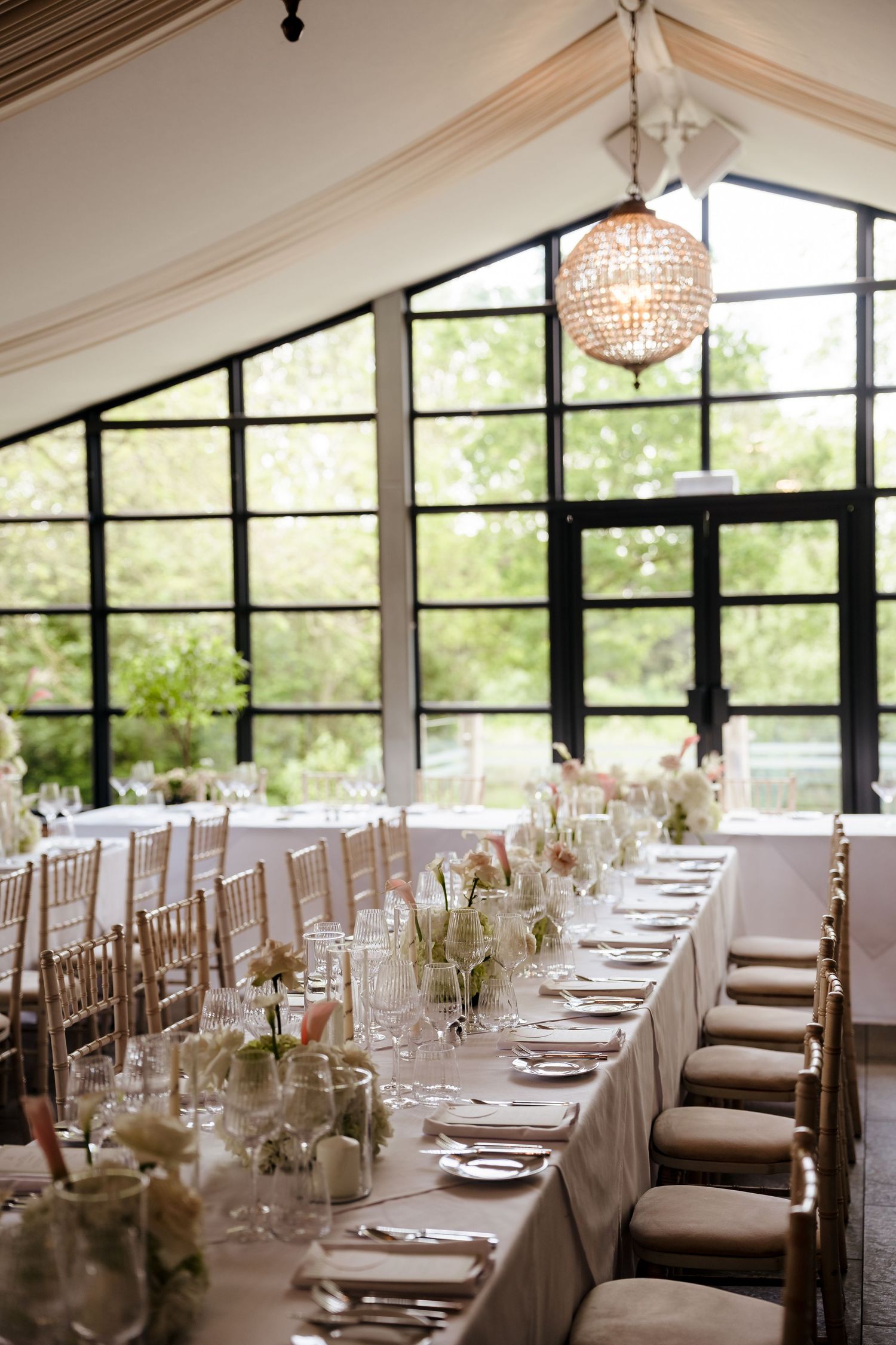 Elegant wedding reception hall with long dining table, chiavari chairs, floral centerpieces and globe chandelier.
