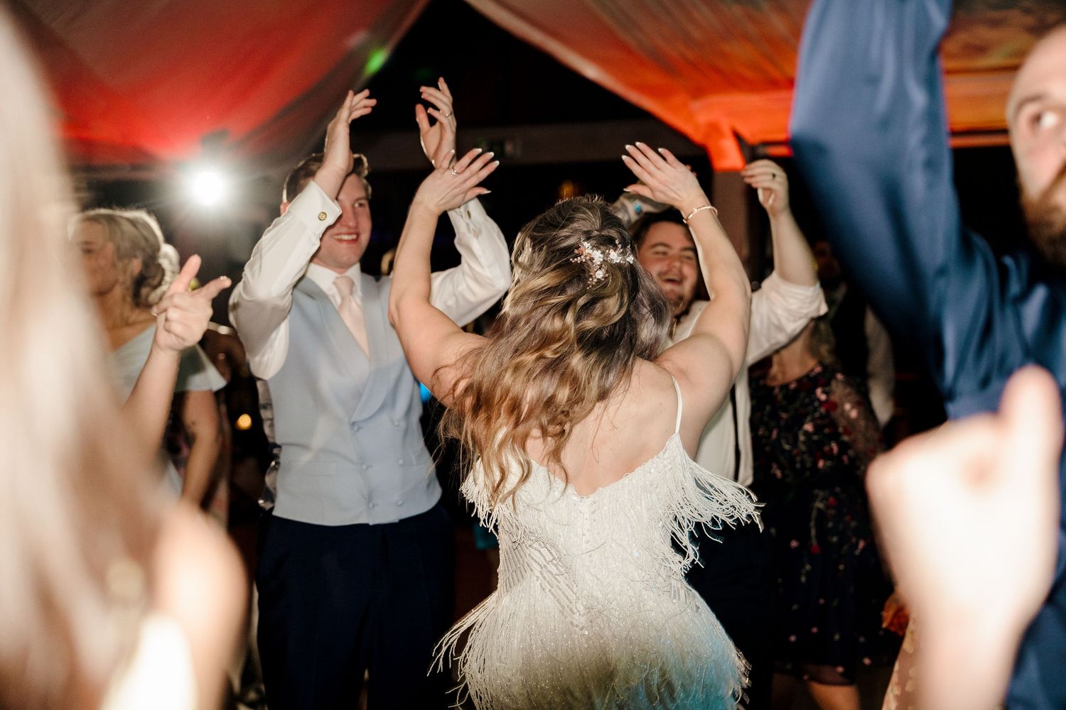 Bride in a feathered dress dancing joyfully with guests on a lively wedding dance floor.
