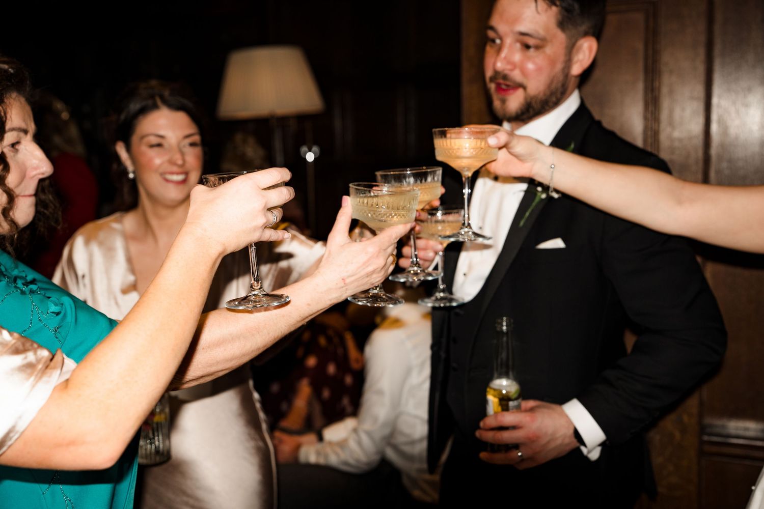 Groom and guests raise cocktail glasses in a celebratory toast at a wedding reception.