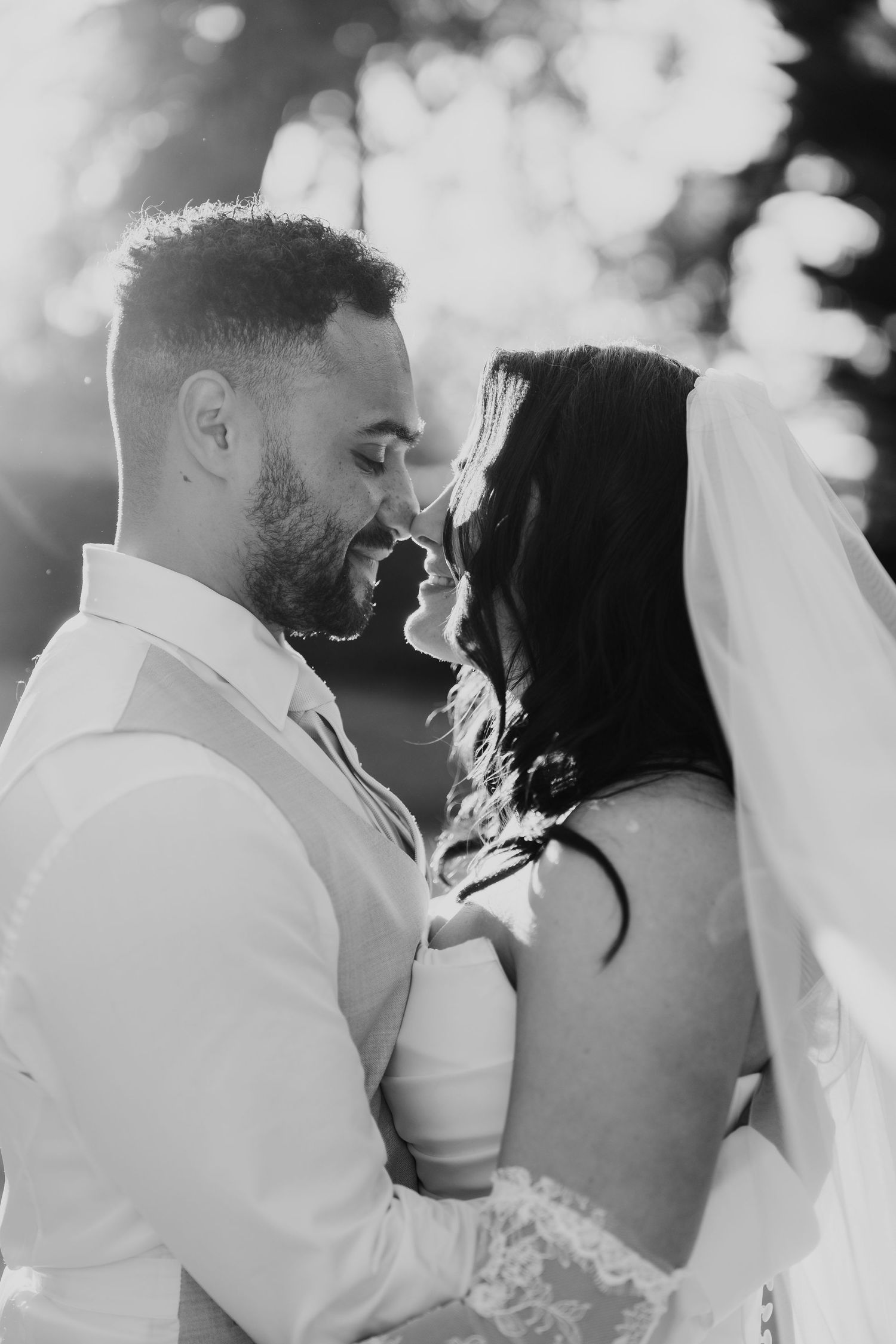Black and white romantic portrait of bride and groom nearly kissing with bokeh light background.