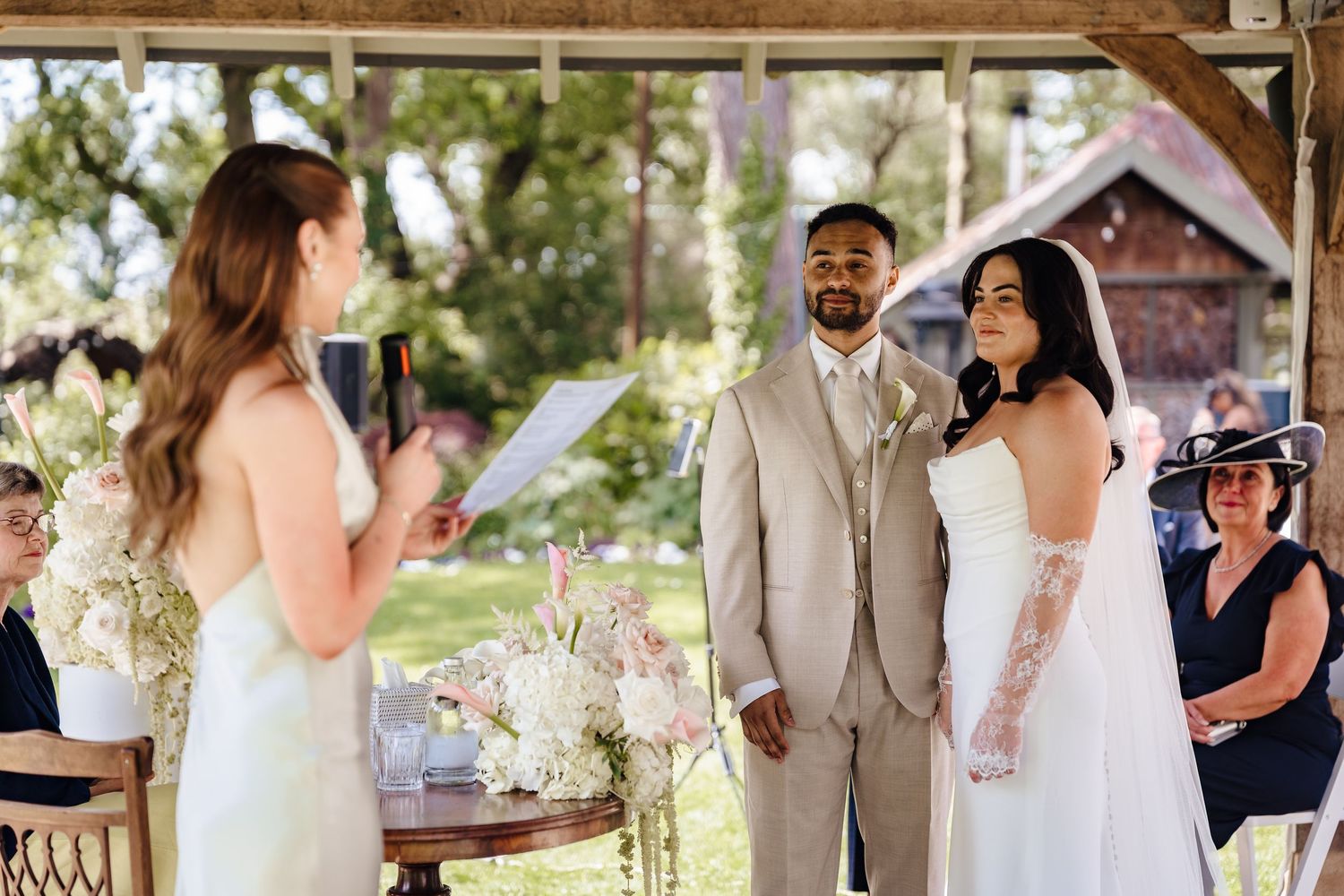 Bride and groom exchanging vows at outdoor wedding ceremony under wooden gazebo.