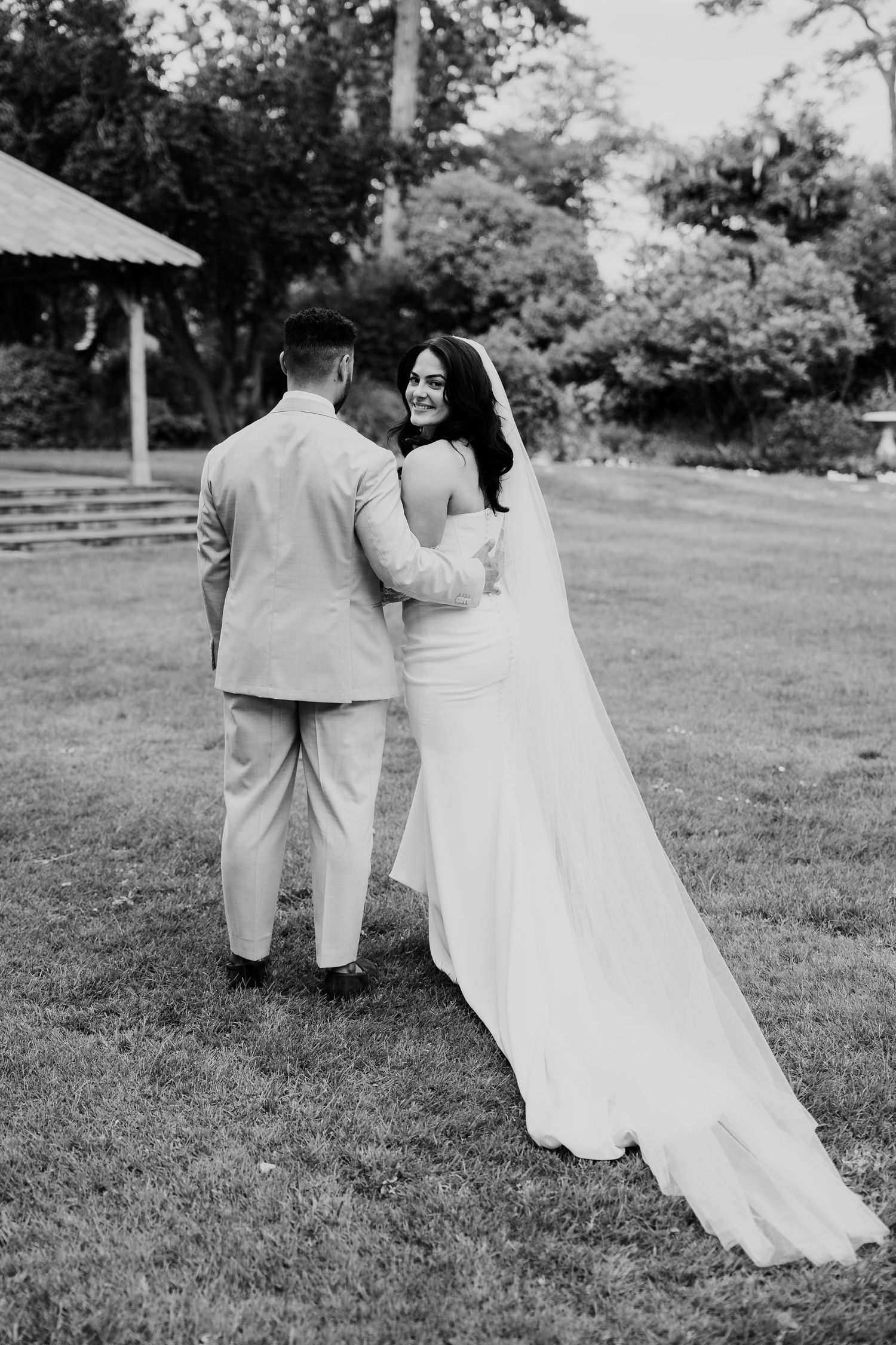 Bride and groom walking hand in hand on green lawn in black and white wedding portrait.