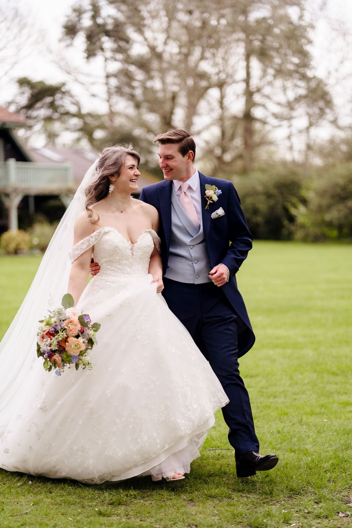 Smiling bride and groom walking together on a lawn, bride holding a colorful bouquet.