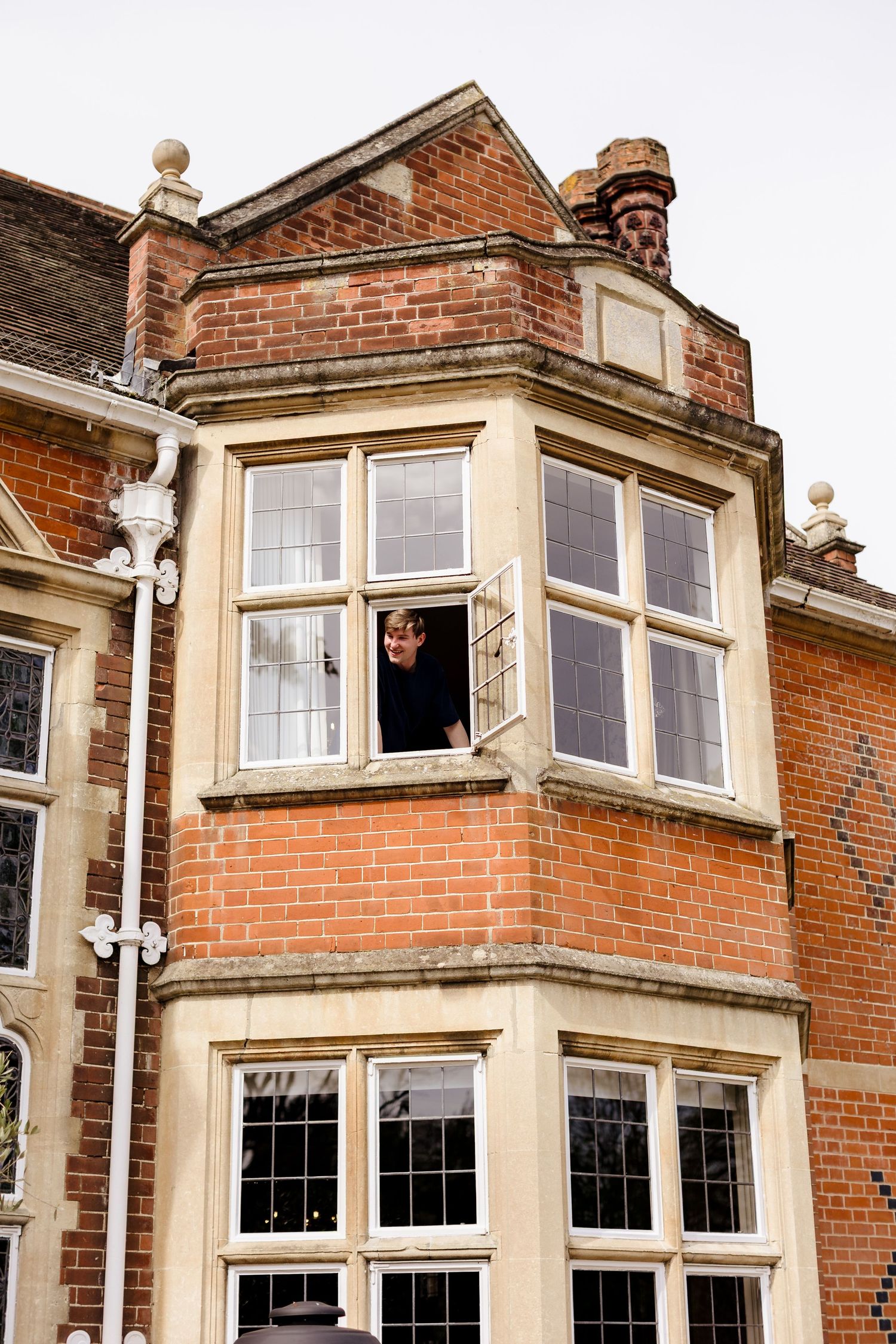 Person leaning out of a bay window of a traditional red brick English manor house.