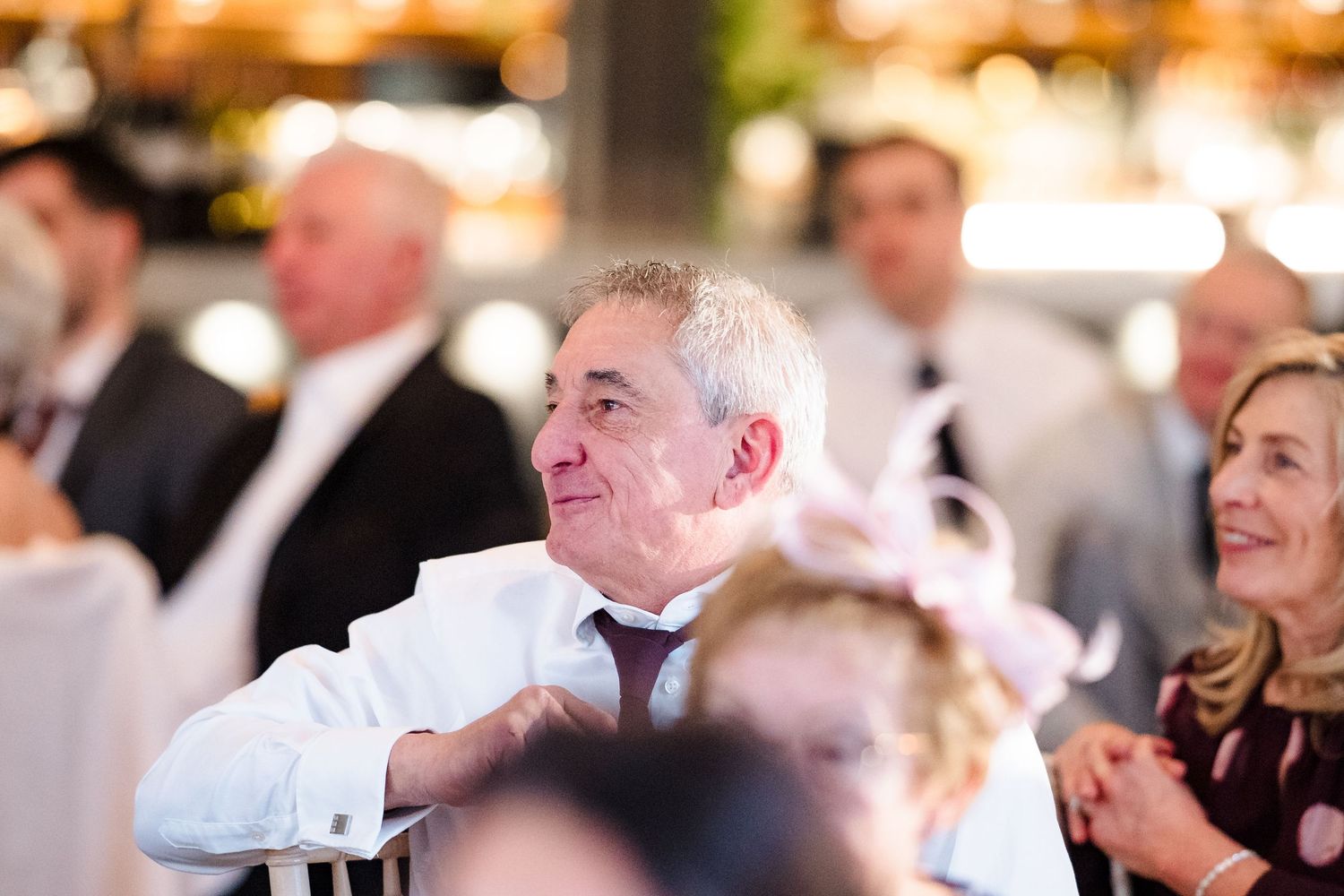 Wedding guest in white shirt smiling and laughing during the reception speeches at a wedding.