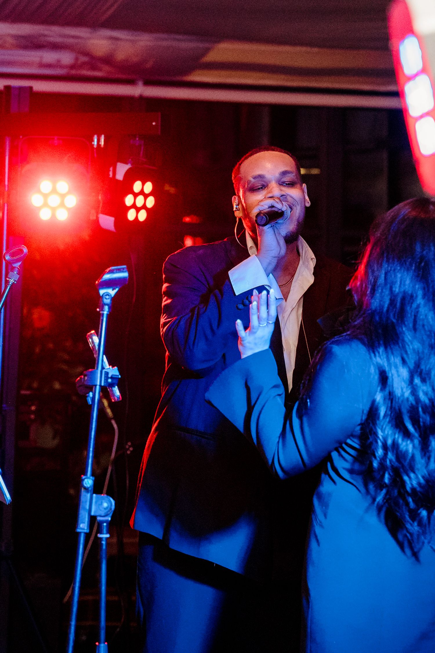Energetic live wedding band performer singing on stage under dramatic red and blue stage lighting.