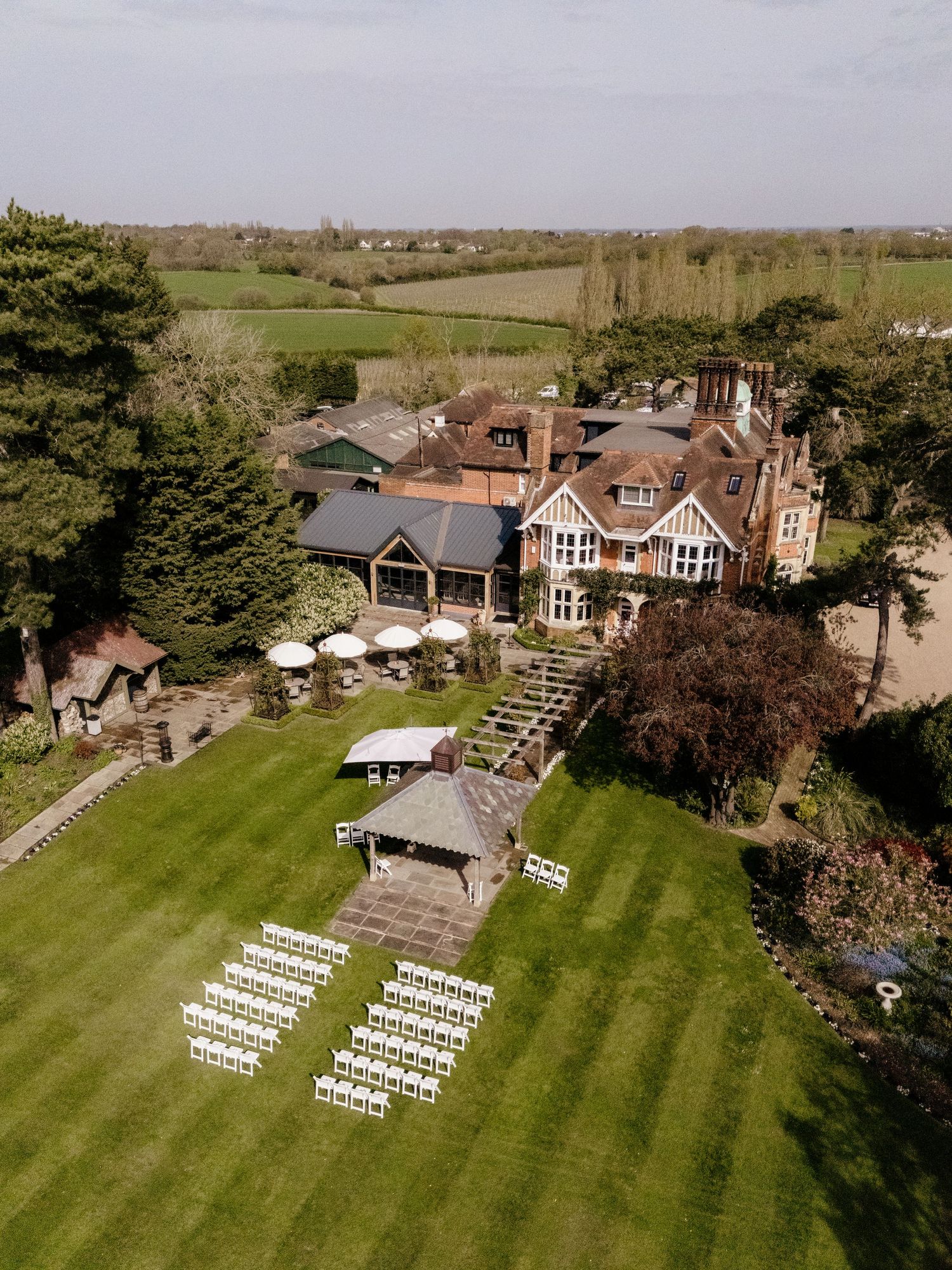 Aerial view of a countryside wedding venue with white chairs arranged on a manicured lawn.
