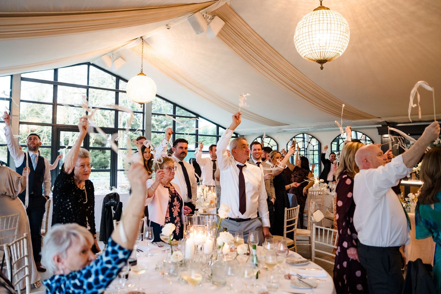 Wedding guests raise glasses in celebration inside a beautifully decorated marquee reception venue.