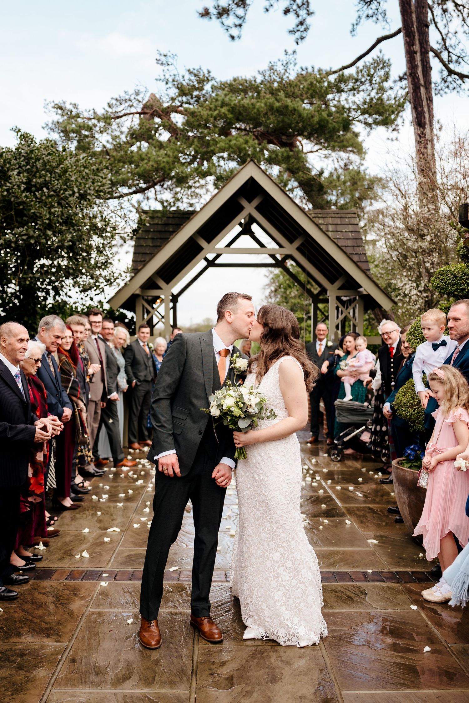 Bride and groom share a kiss at the altar during an outdoor wedding ceremony with guests lining the aisle.
