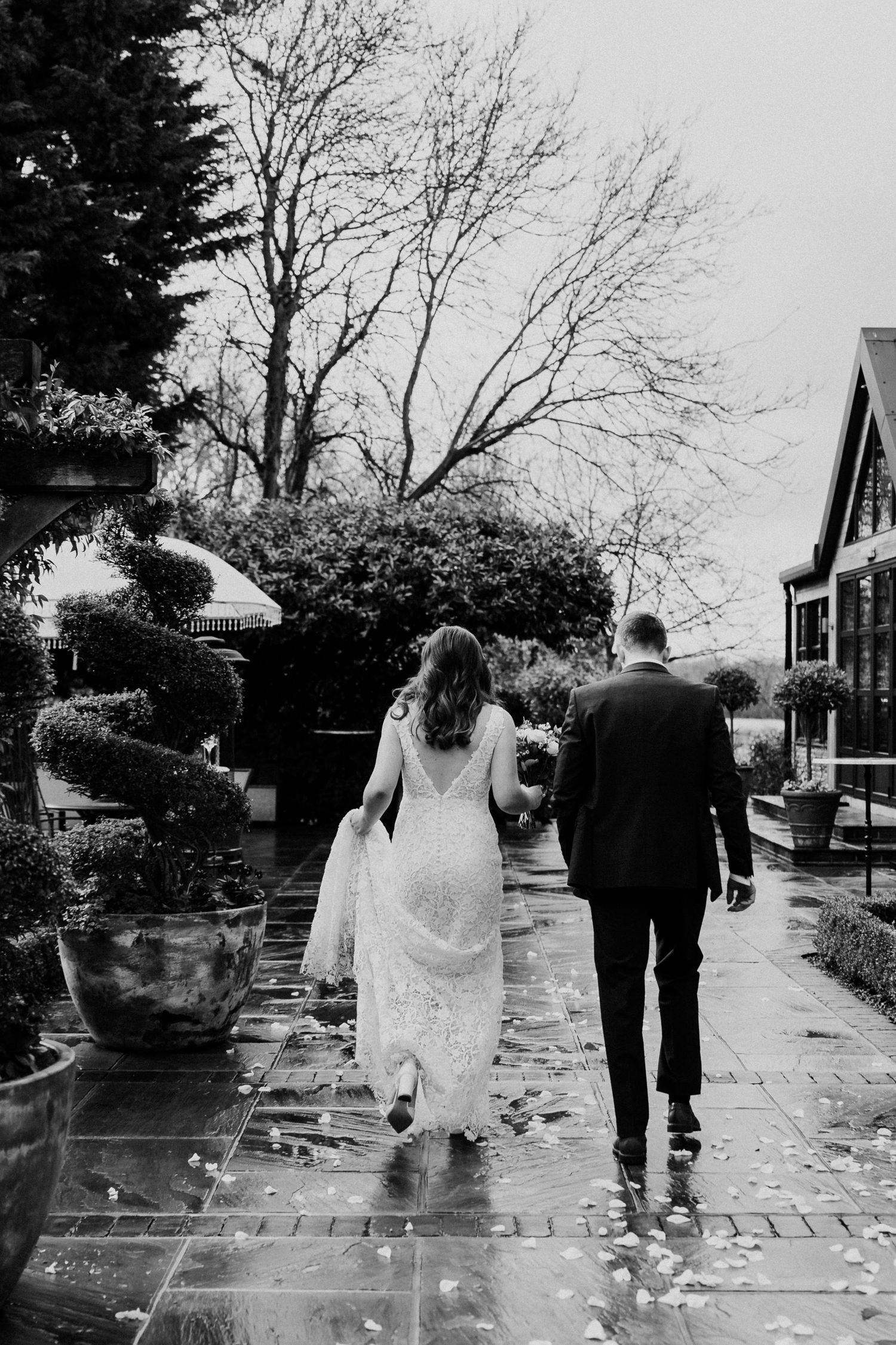Bride and groom walk hand in hand along a wet patio path in black and white wedding photo.