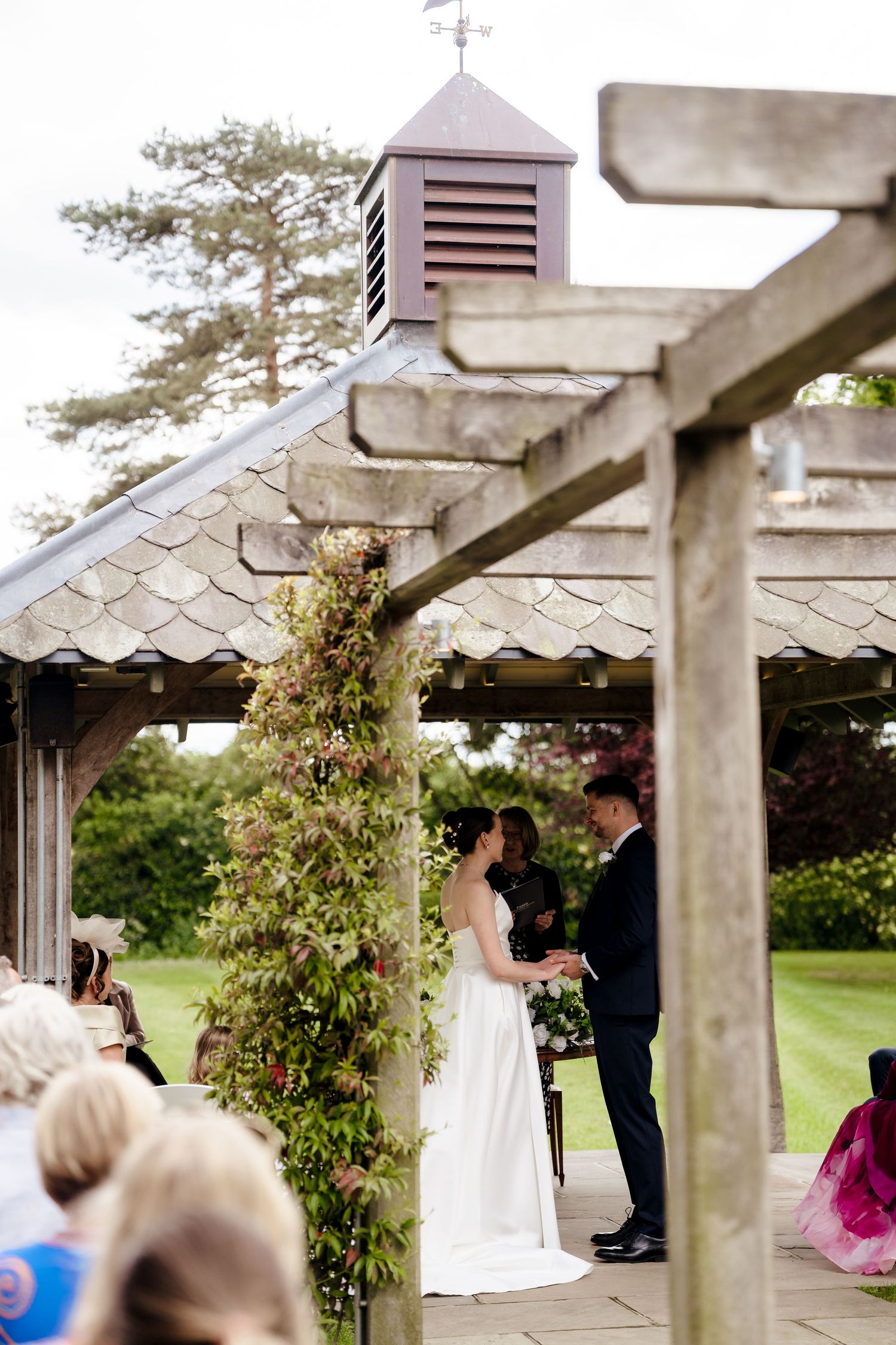 Bride and groom exchange vows under a floral-adorned pergola at an elegant outdoor garden wedding ceremony.