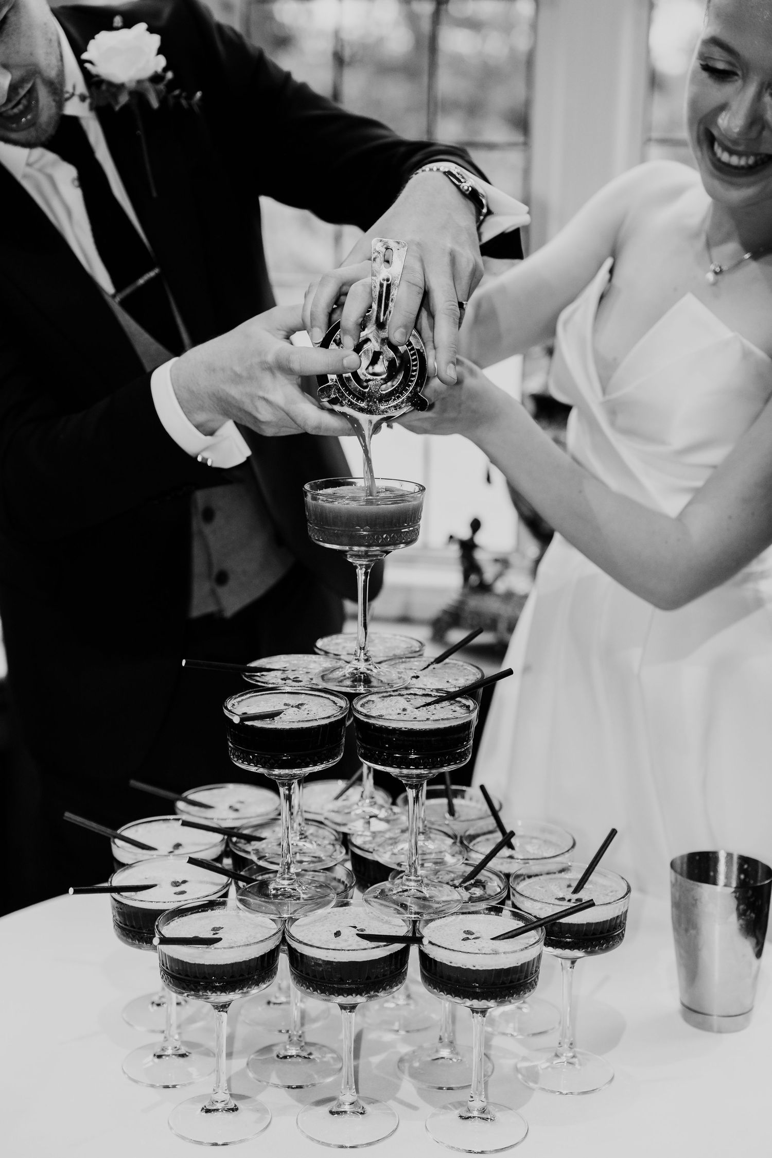 Black and white photo of bride and groom pouring champagne tower at wedding reception.